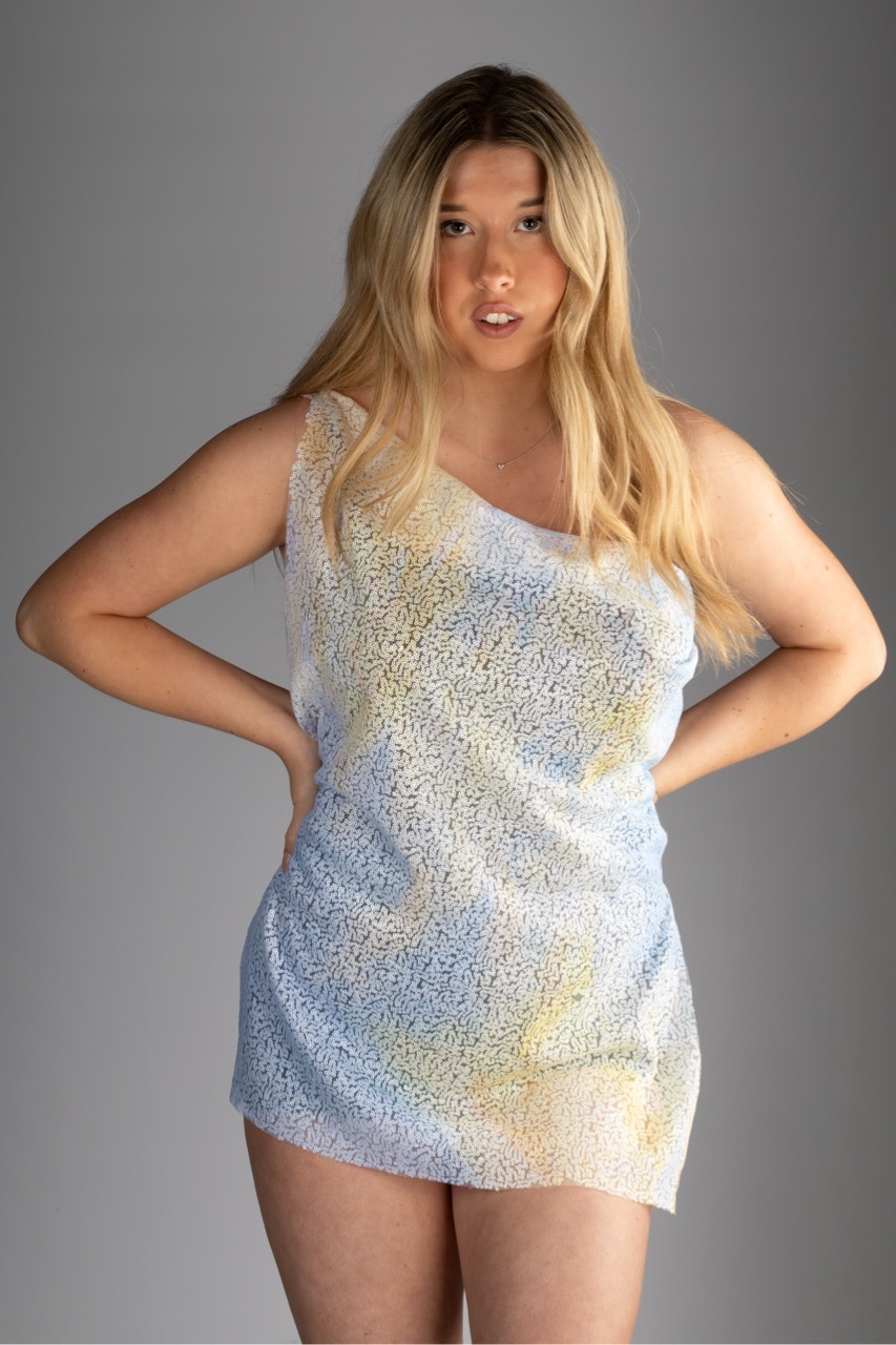 Blonde woman in sparkly silver sequined mini dress with hands on hips against grey background.