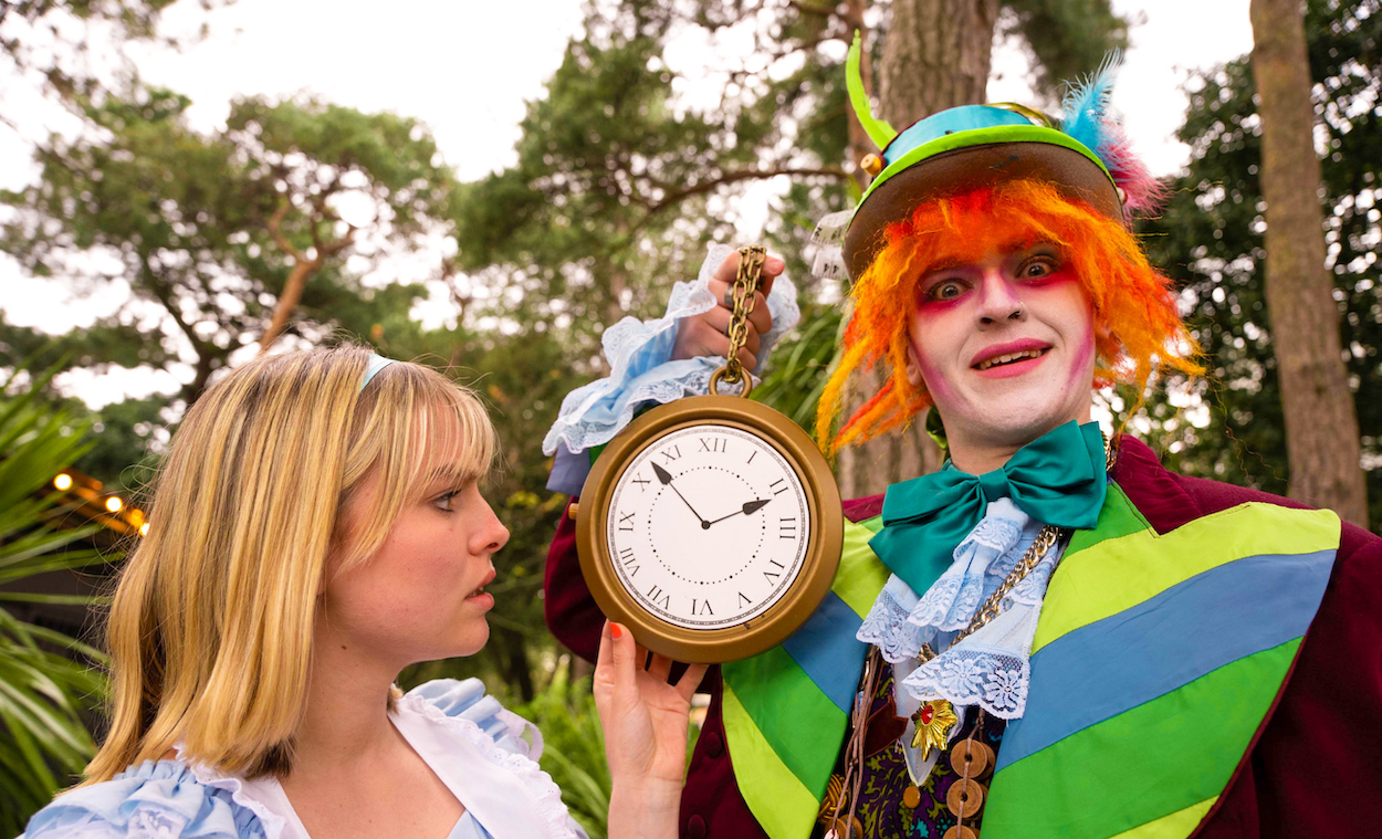 Two people in costume as Alice and the Mad Hatter from Alice in Wonderland. The Mad Hatter is holding a large watch, which Alice is looking at.