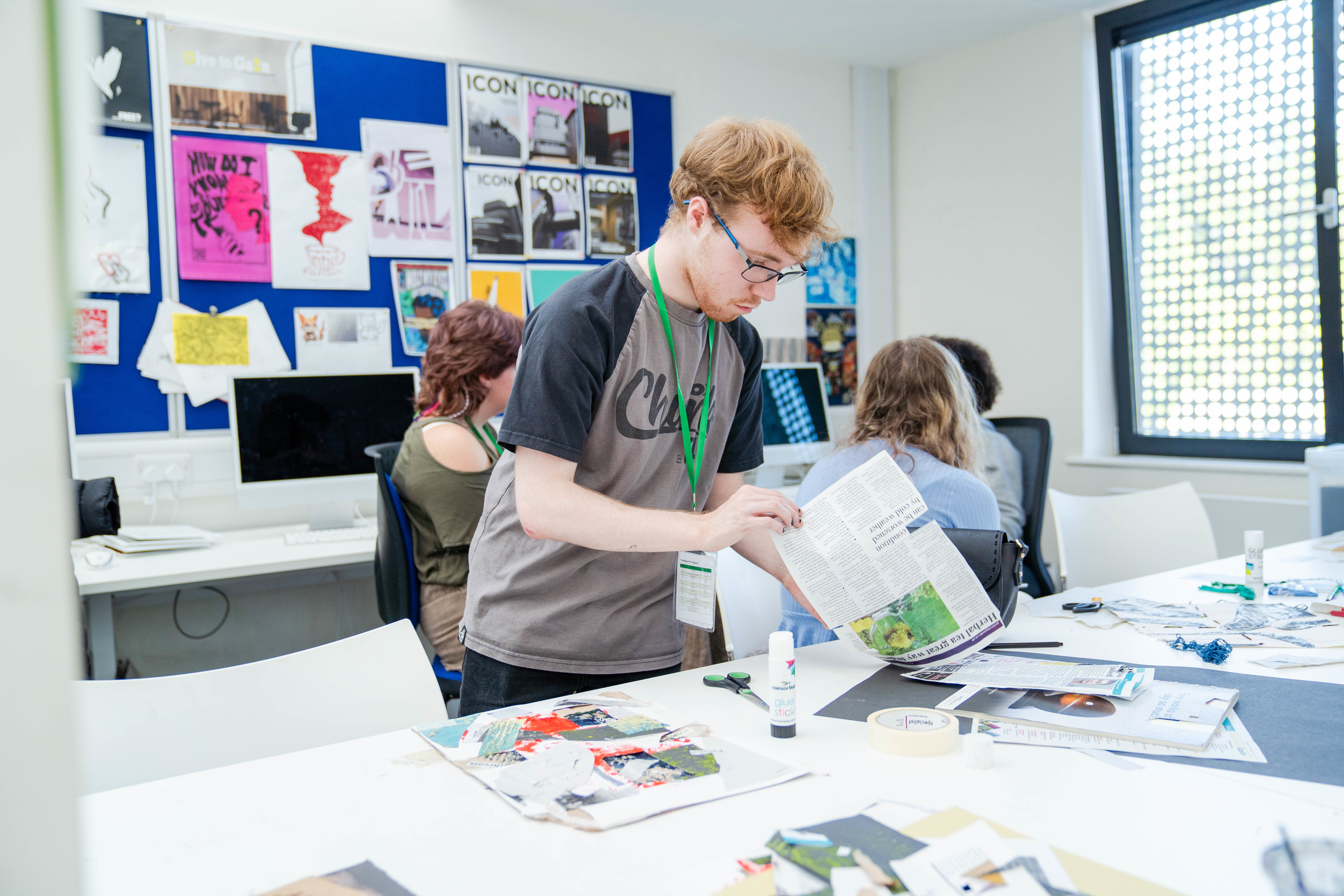 Student stood at work table looking through images for collage art piece