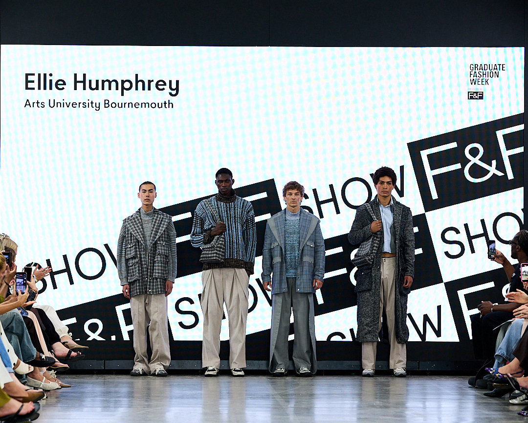 Four male models stand on a fashion runway wearing layered grey outfits, with Ellie Humphrey Arts University Bournemouth displayed on the backdrop and audience seated on both sides.
