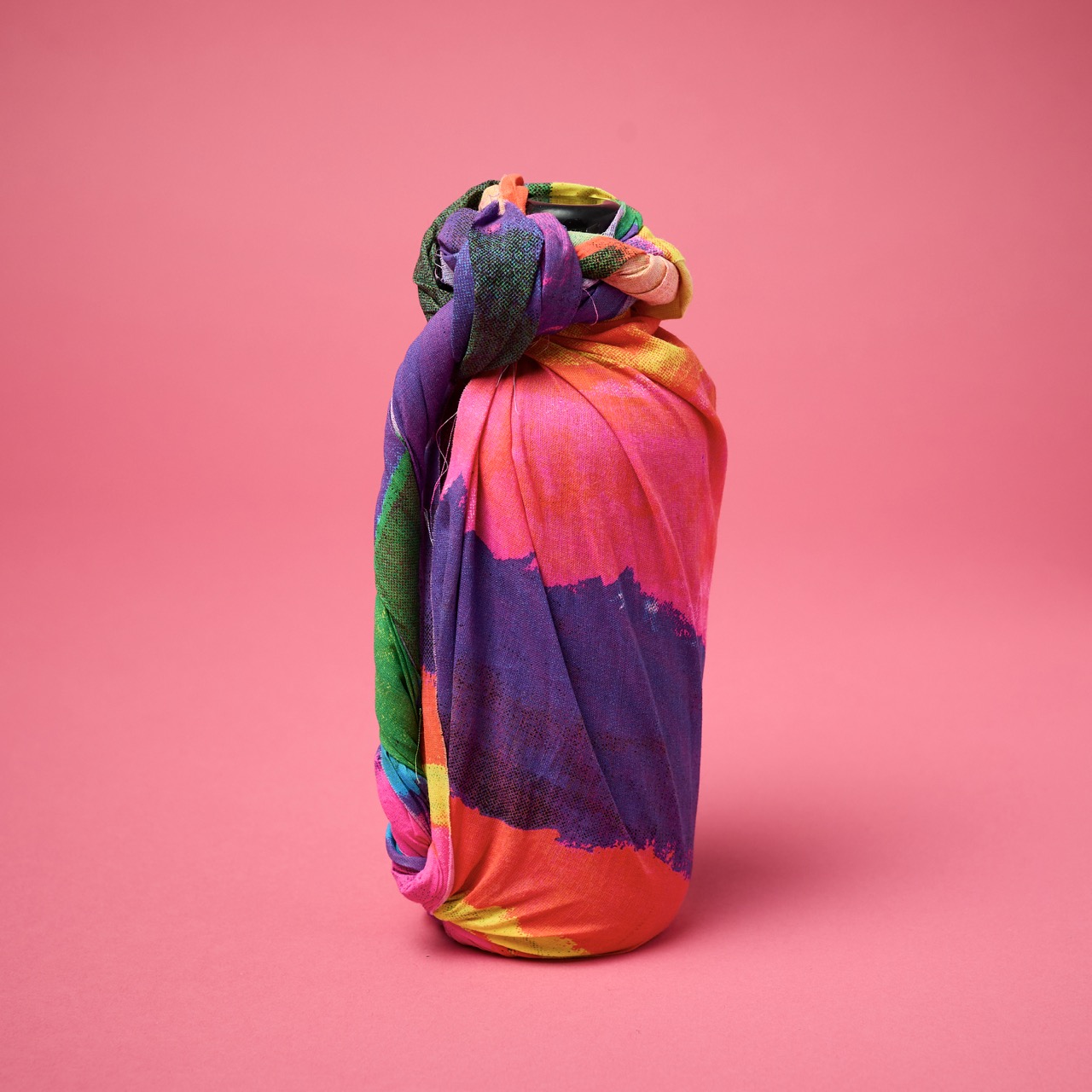 Multicoloured, pattered Lush Knot Wrap on a bright coral pink/red background.