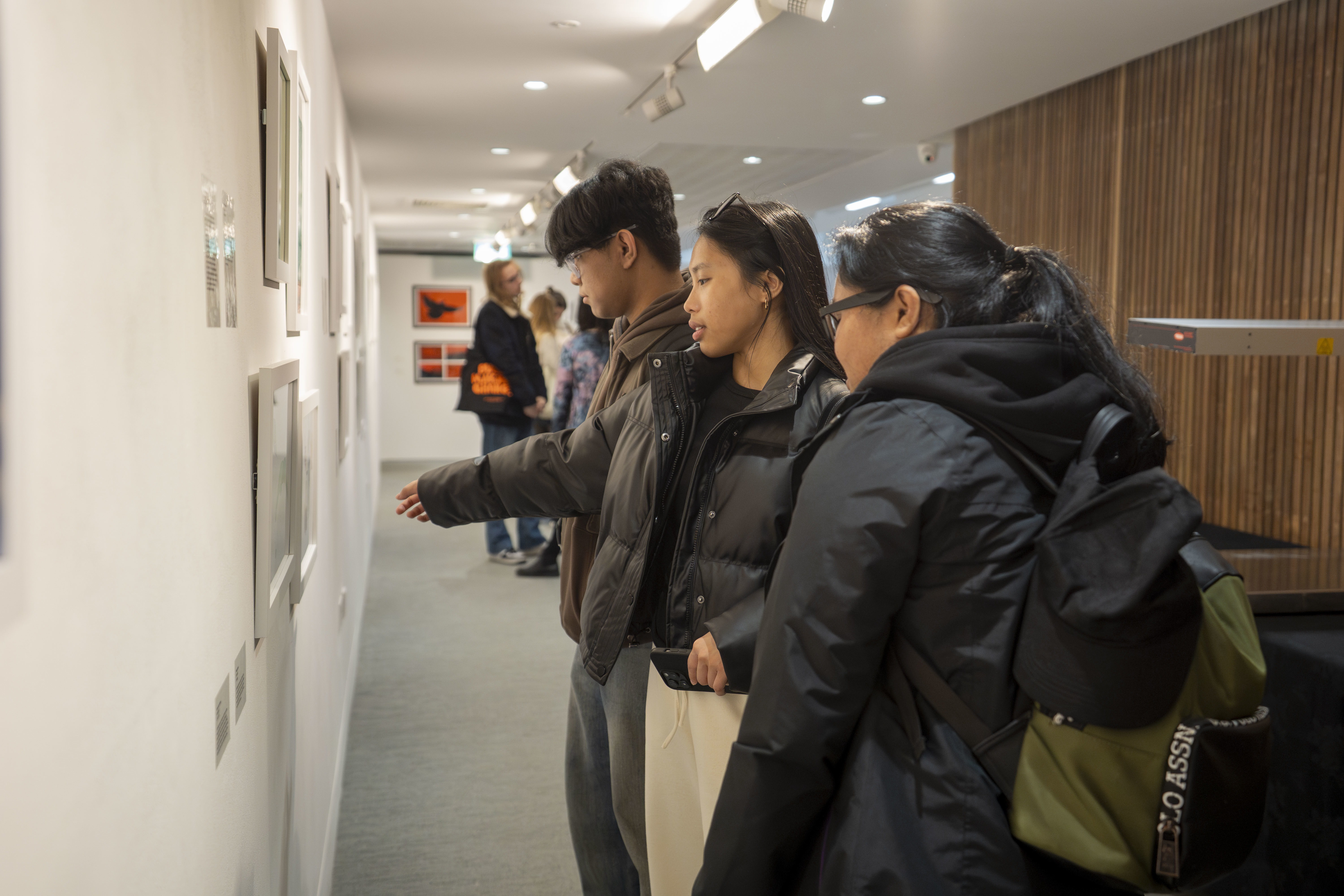 Three students looking at their artworks displayed on the wall in an art gallery