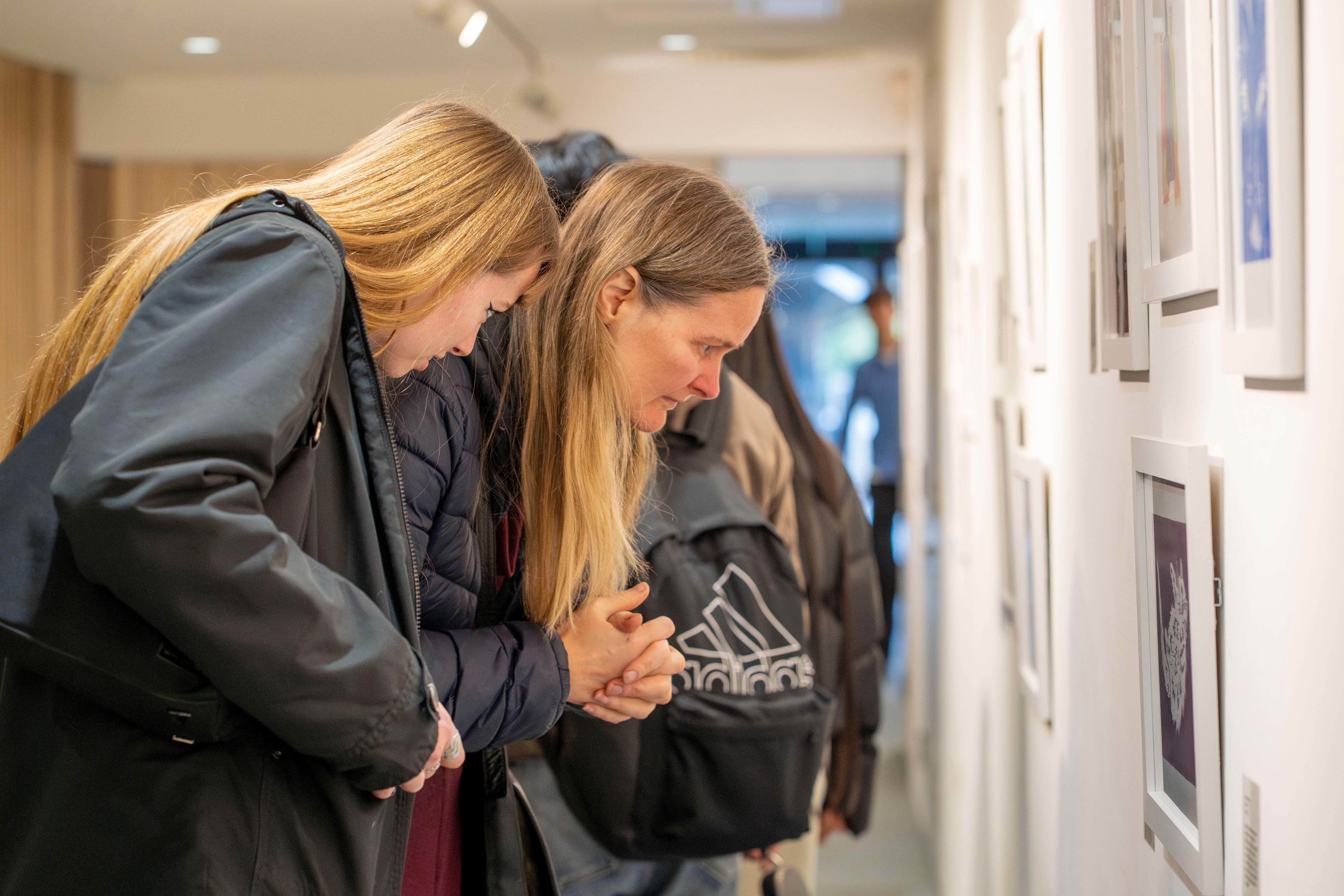 Two people looking closely at artwork on display in TheGallery.