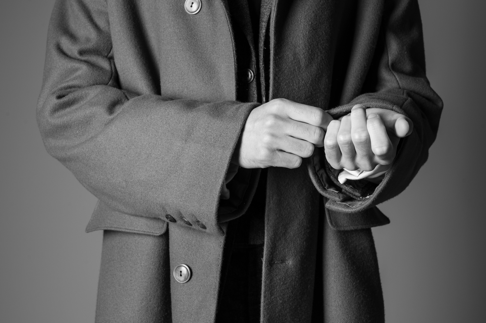 Person in dark coat, black and white image showing torso and hands only.