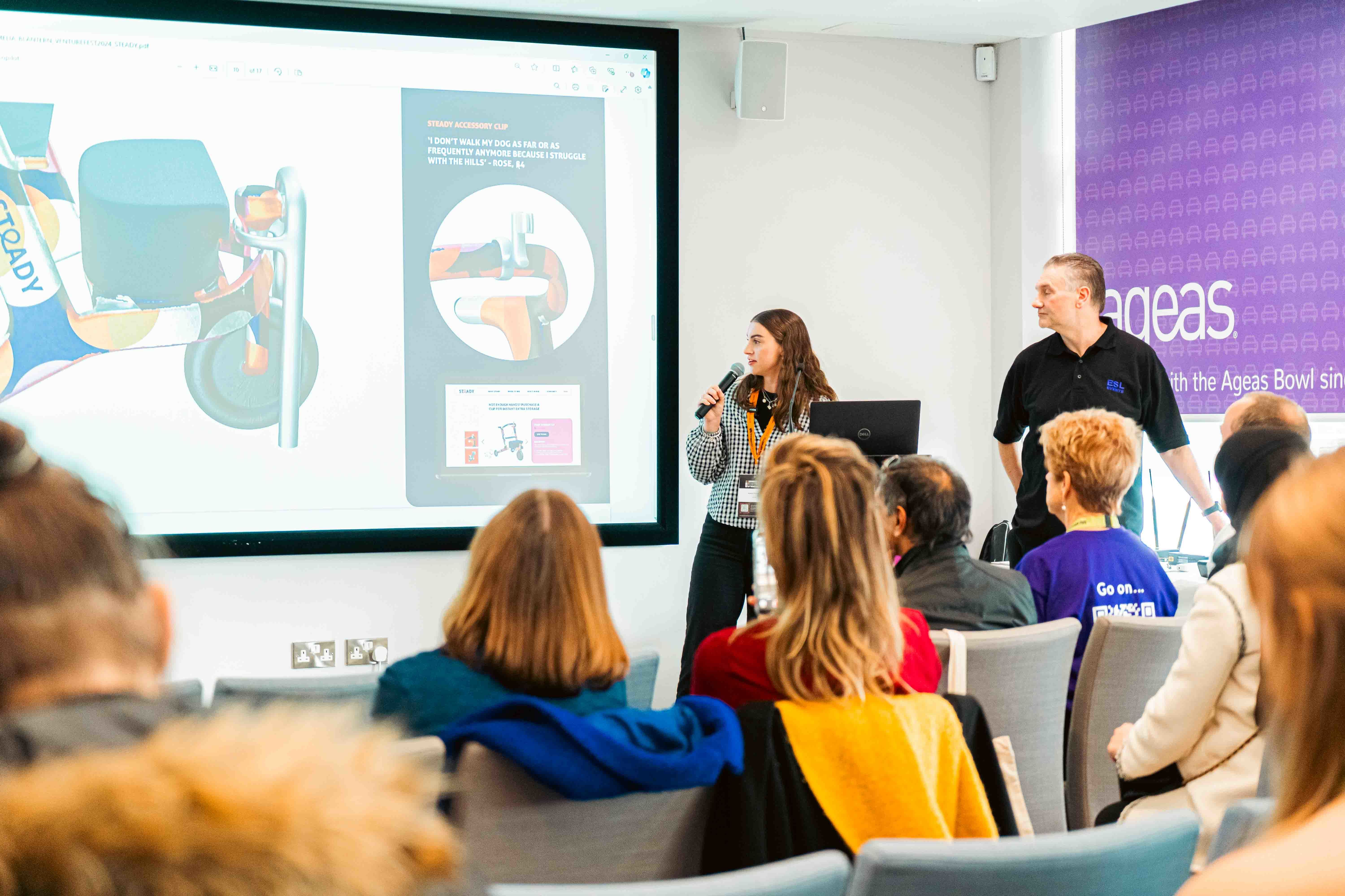 A. Blantern holding a microphone while giving a presentation about her project 'Steady' in front of attendees at Venturefest South 2024.