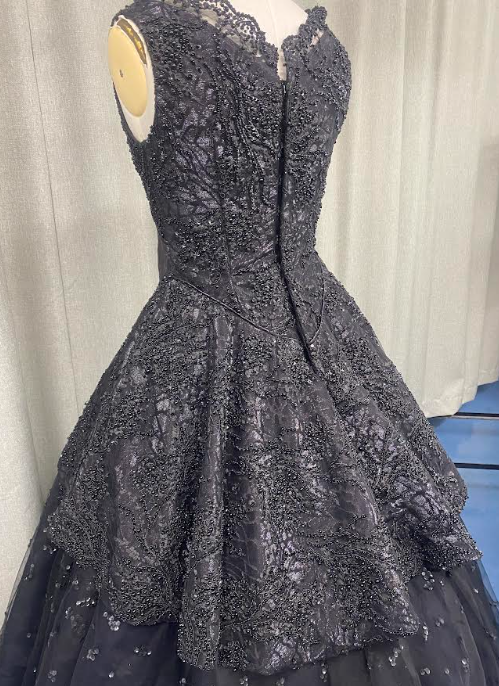 Black sequined ball gown on mannequin with fitted bodice and full skirt, displayed against white curtain backdrop.