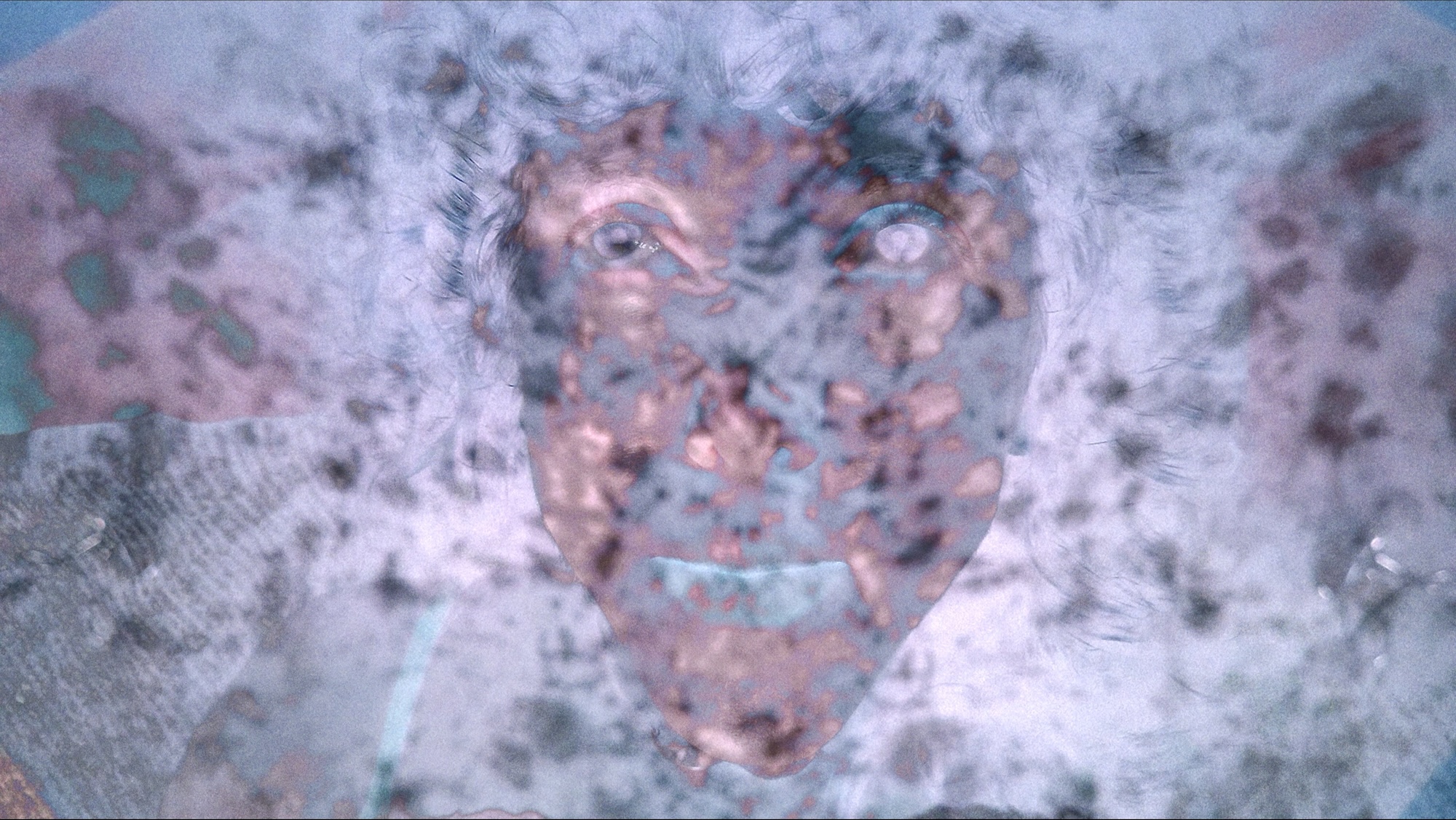 A close-up of a painted face with blue eyes and a smiling mouth, shown against a mottled grey and pink background.