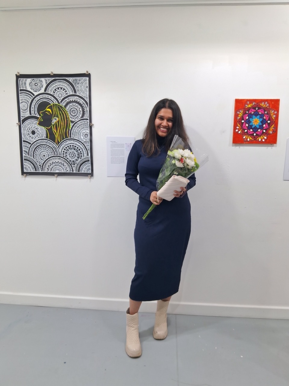 Ananta stood by her painting work at the exhibition in a dress, holding a bouquet of flowers.