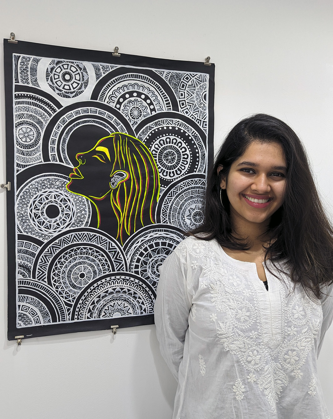 Ananta Sharma stood by her work in the BUG gallery, showing a yellow outlined woman with circle patterns, black background.