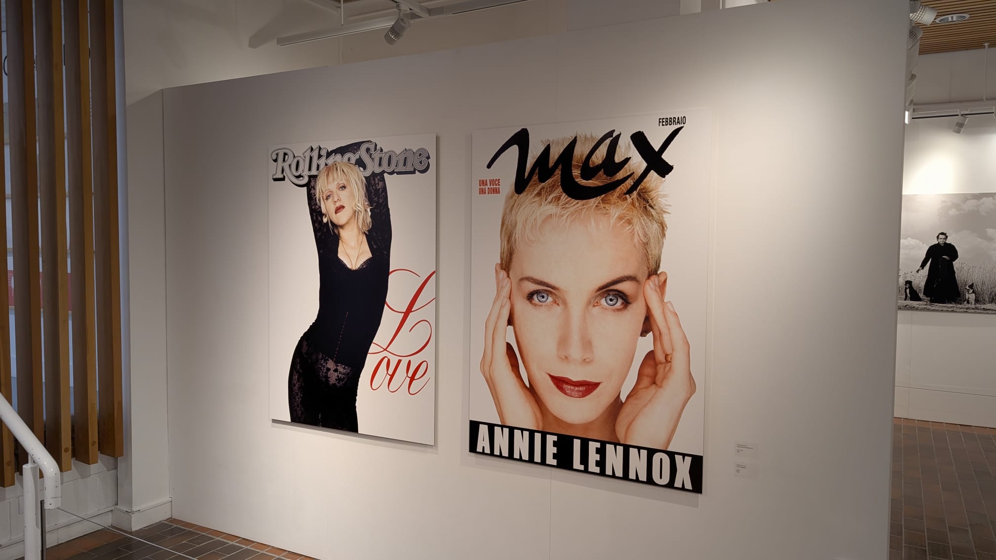 Two Annie Lennox posters hang on a white gallery wall, including one with a close-up portrait titled "Max" and another full-body image with "Love" text.