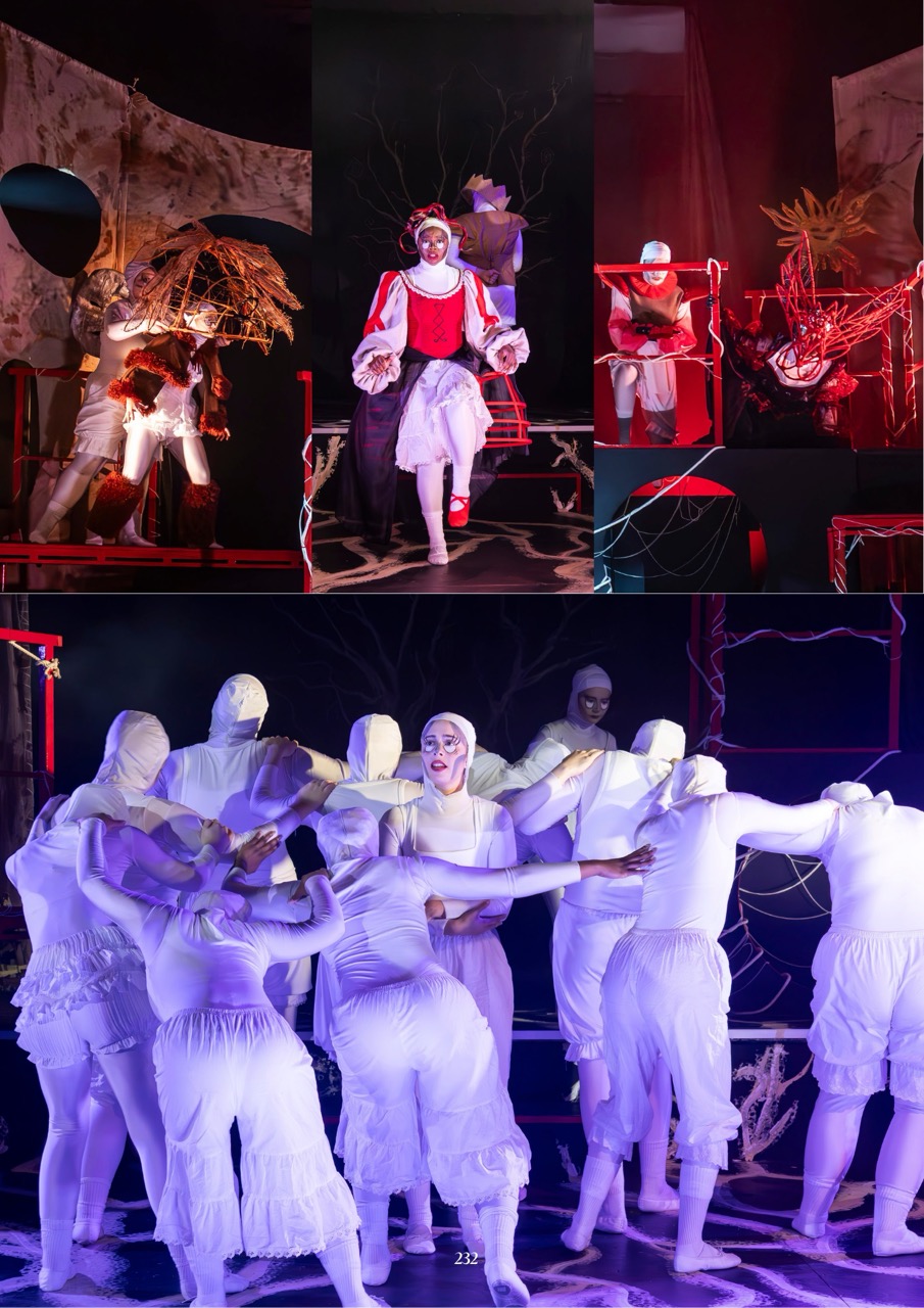 A theatrical stage performance features a central performer in white and red costume, with several masked dancers in white costumes gathered below under red and purple lighting.