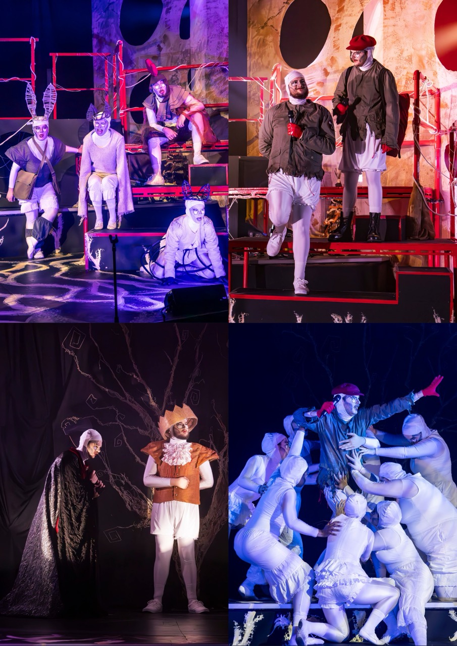 Actors in theatrical costume stand and sit on a stage with red metal frames and coloured lighting, while other performers in white-painted outfits cluster around a central figure.