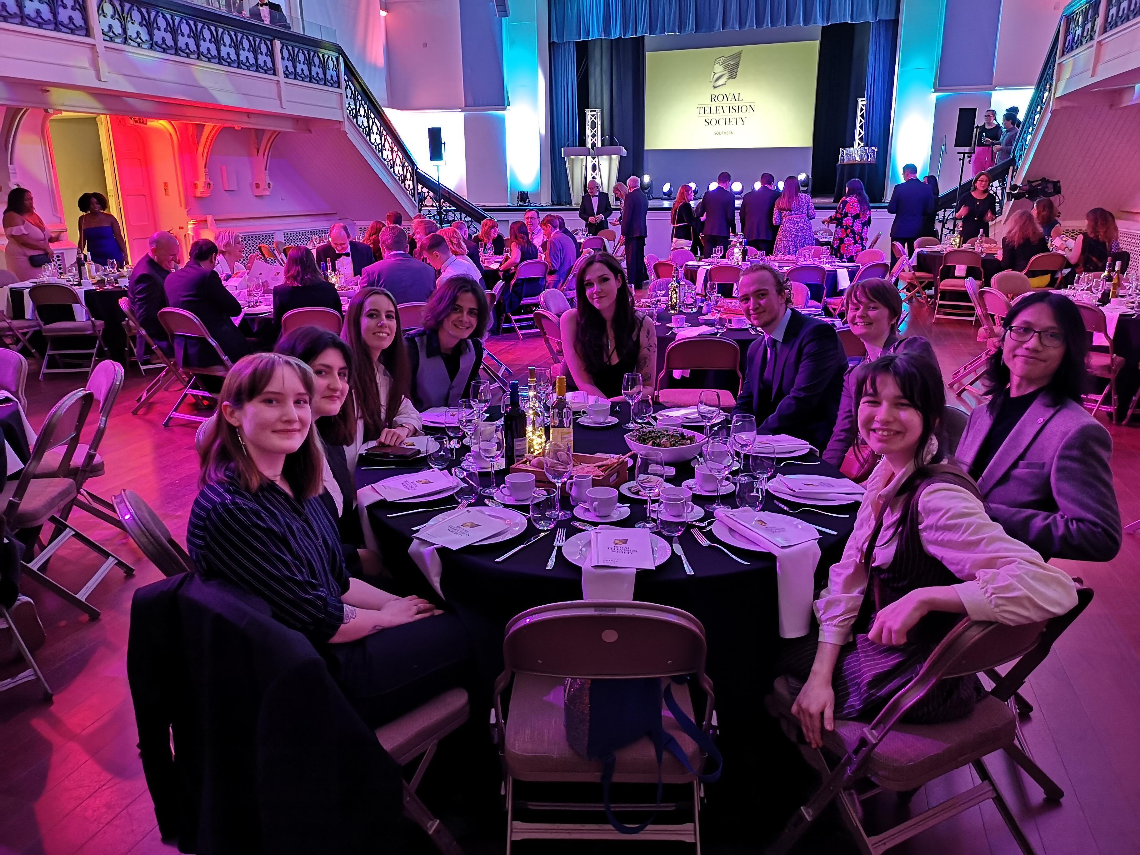 A group of nine people sitting around a table at an awards ceremony.