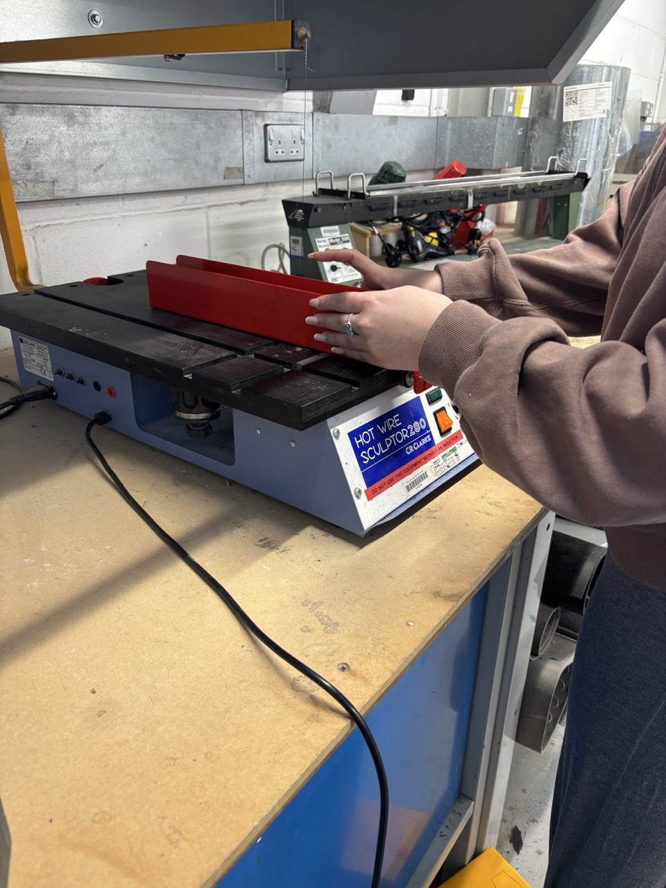 Student interacting with a hot wire sculptor, moving a red piece of material over it.