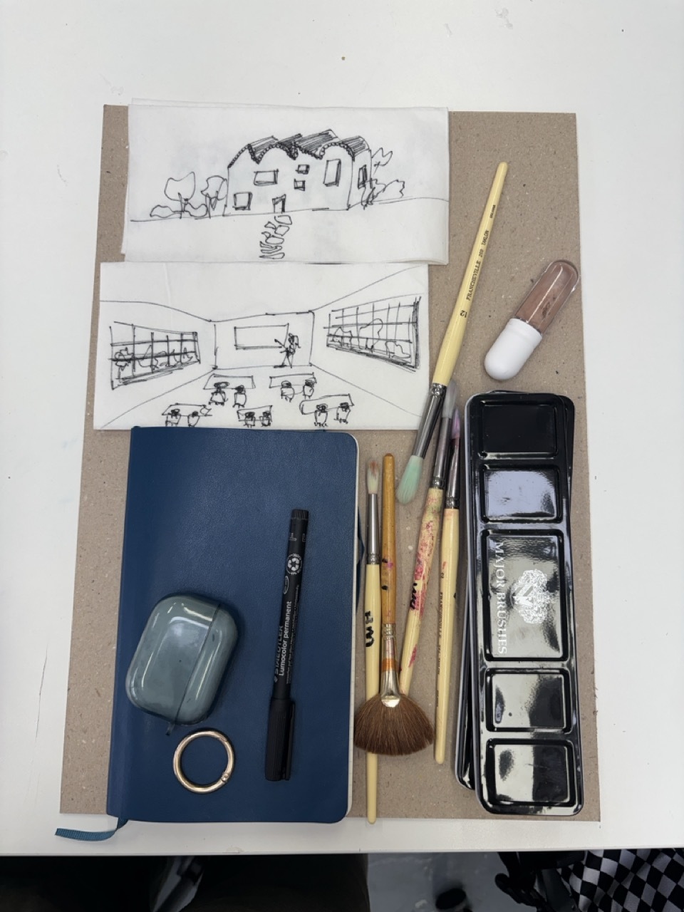 Small building sketches next to paintbrushes, stationery and a blue notebook.