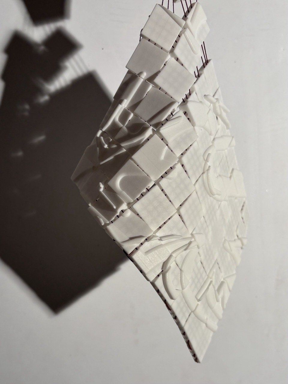 White paper strips woven together in basket-weave pattern with dark shadow cast on white surface.