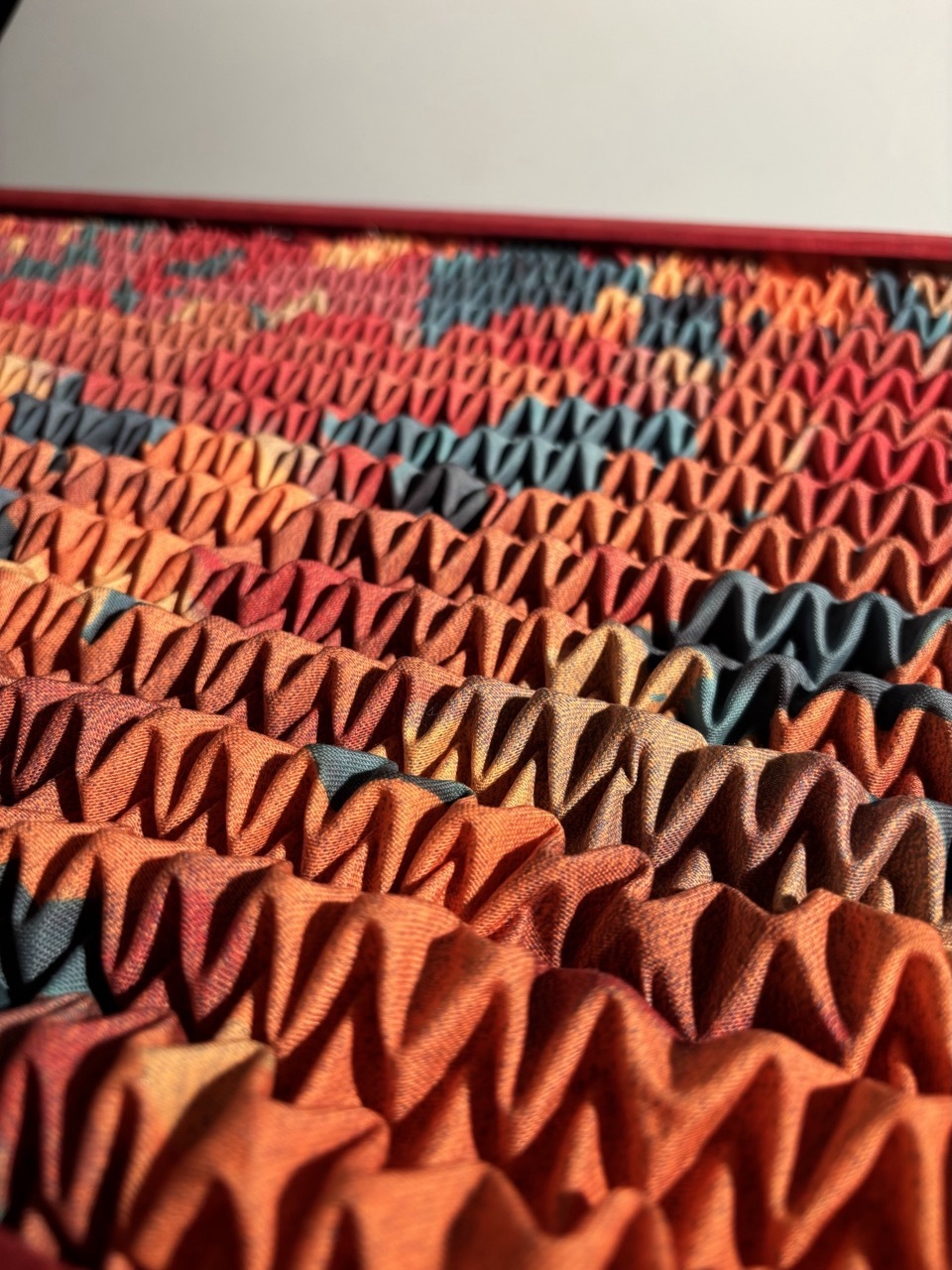 Colourful knitted fabric with zigzag pattern in orange, red, blue, and yellow stripes creating accordion-like pleated texture.