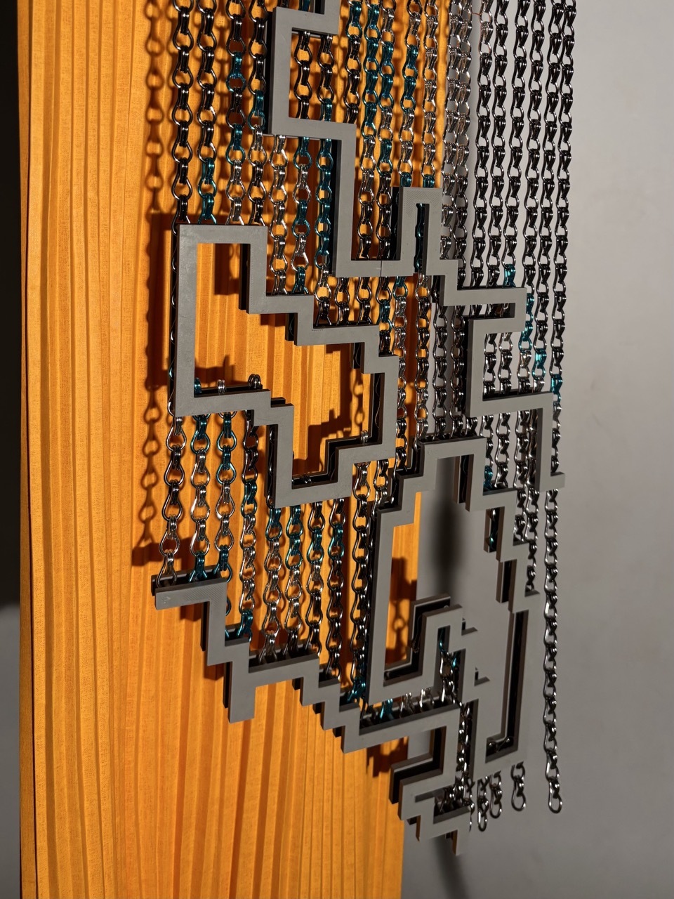 Orange vertical strips transition to grey perforated panels with rectangular cutouts, creating layered geometric pattern against white wall.