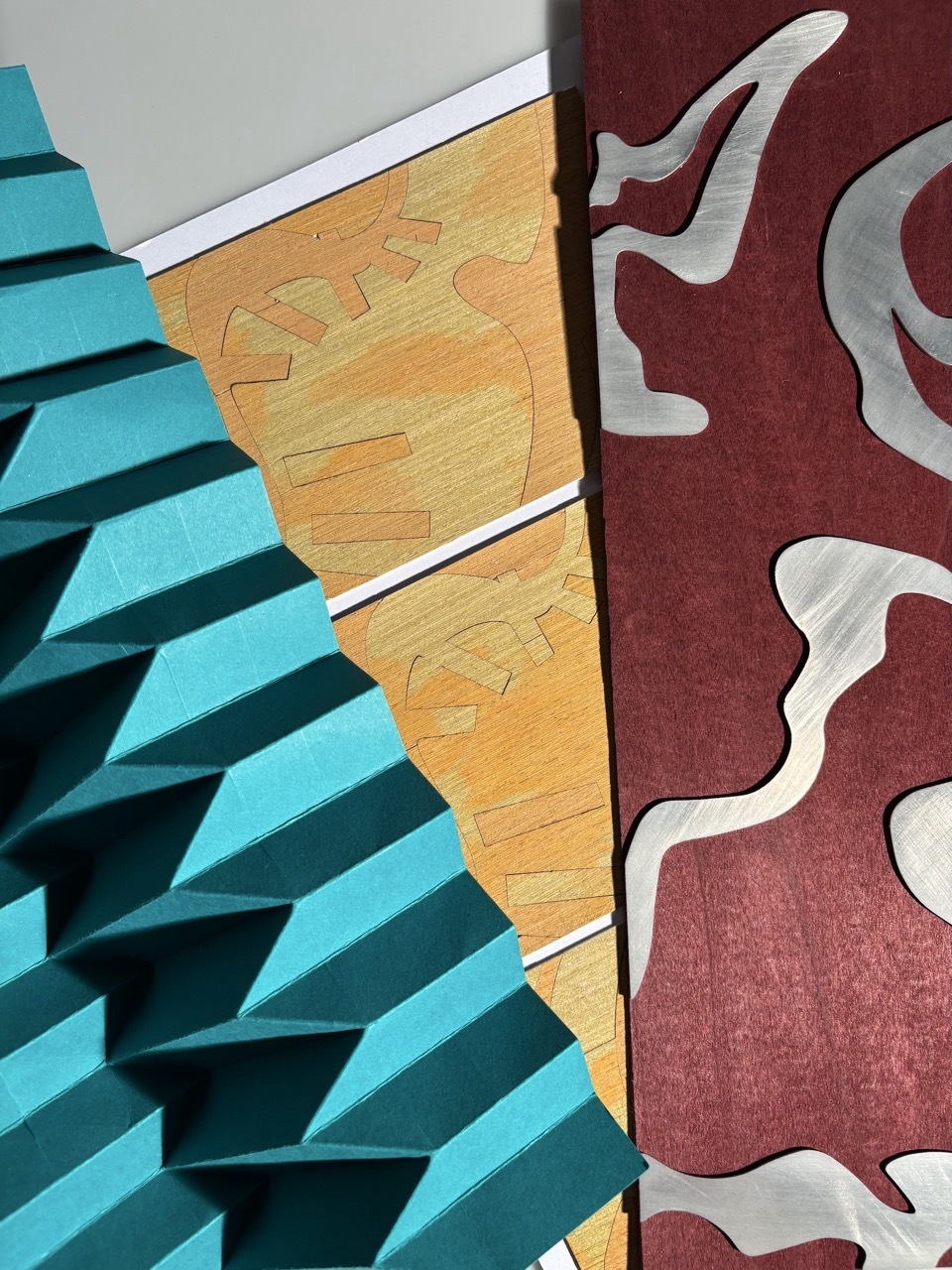 Geometric composition with turquoise angular shapes on left, orange triangular section in centre, and burgundy background with white curved forms on right.