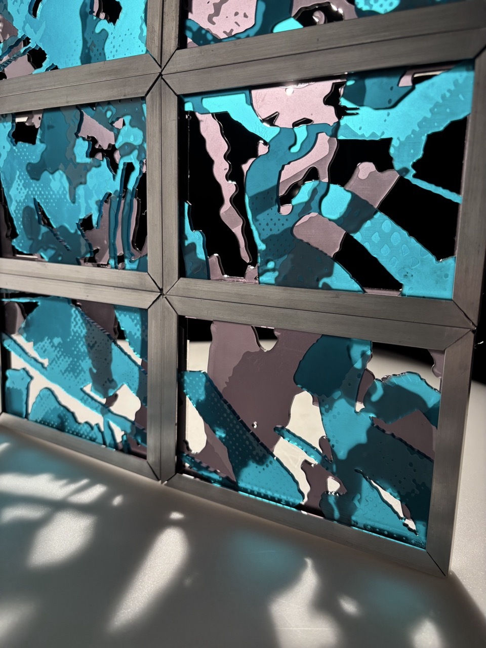 Grey window frame with six panes showing abstract pattern in turquoise, pink, black, and grey irregular shapes.