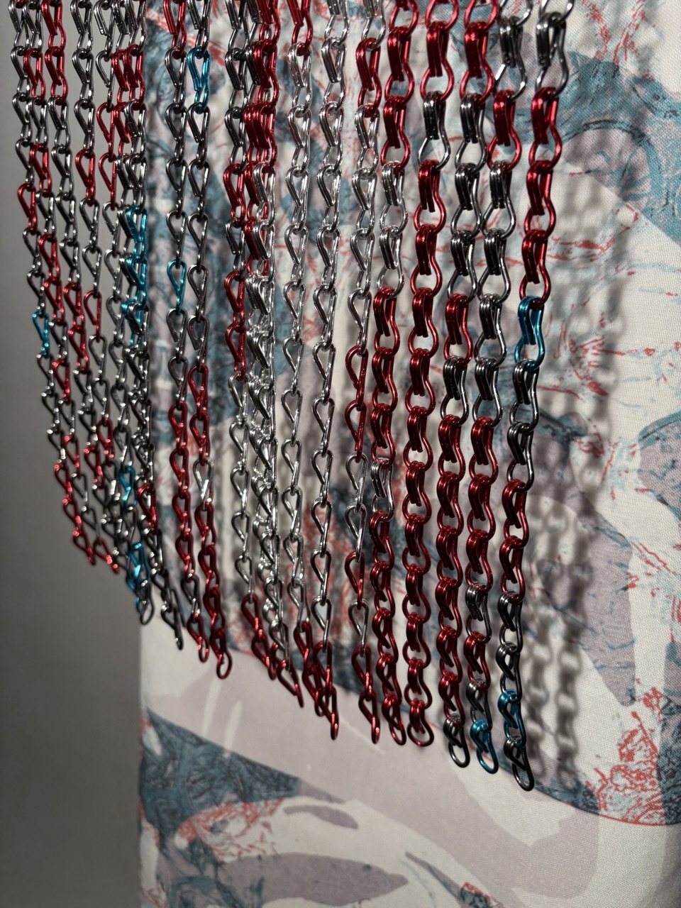 Multiple chains in red, silver, teal, and black hanging vertically against floral wallpaper background with soft lighting.