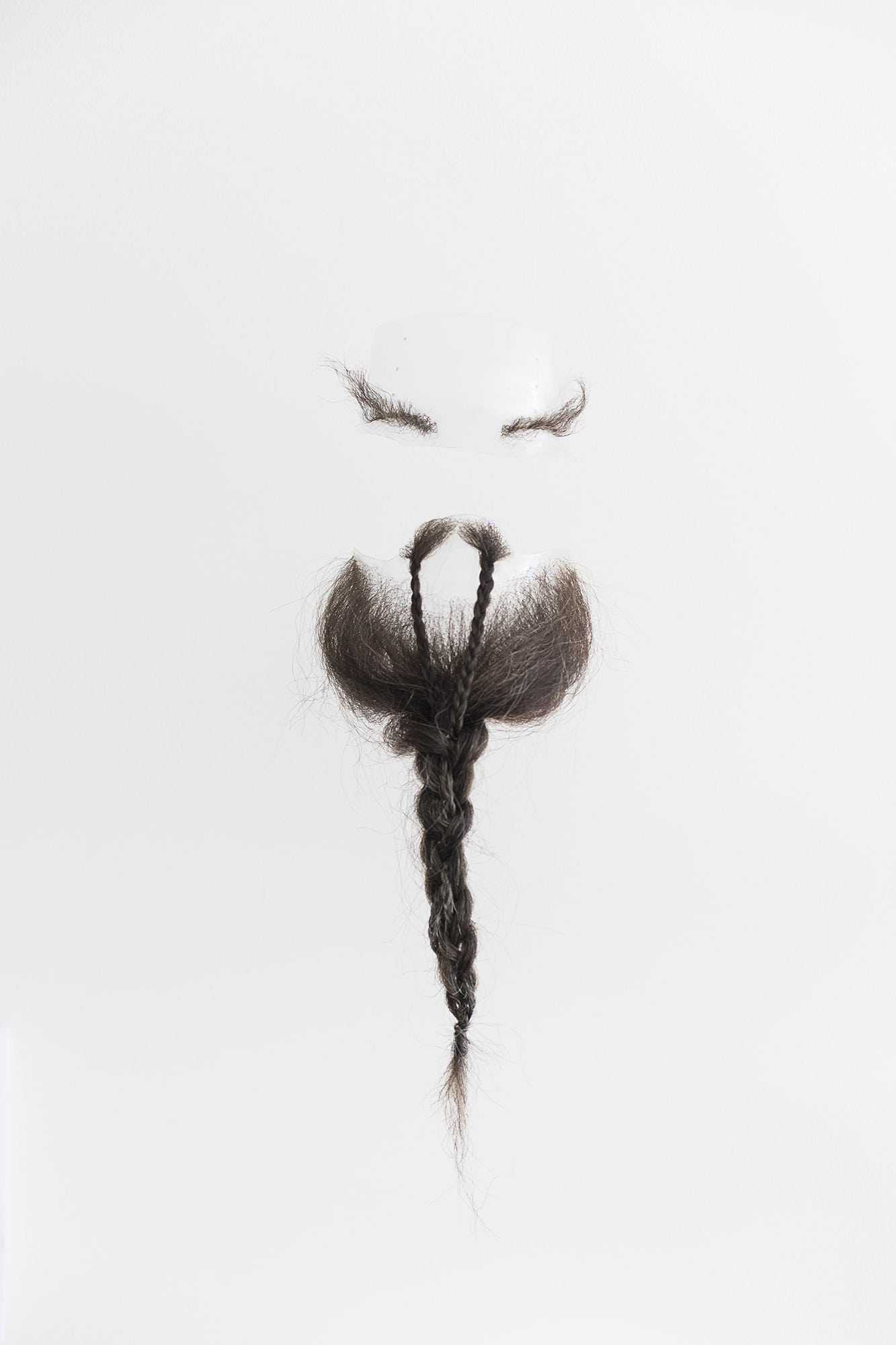 Facial hair prosthetics – a pair of eyebrows, a long plaited moustache and a long plaited beard – on a plain background.