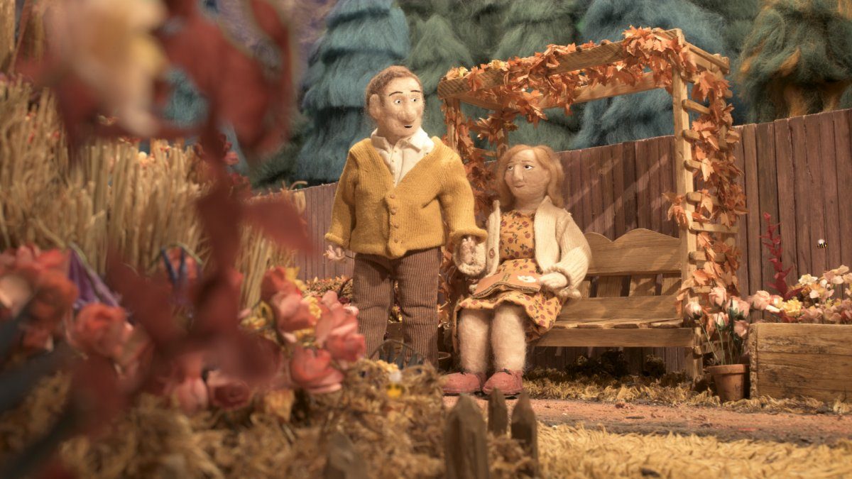 Animation still of a woman sitting on a bench under a trellis, holding hands with a man who is stood up.
