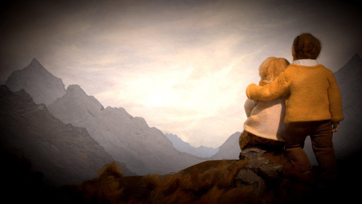 Animated still of a person stood on a mountain side with their arm around another person, looking out at other mountains in the distance.