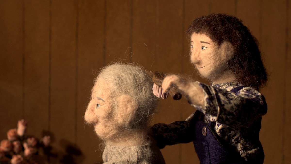 Animated film still showing a woollen girl brushing the hair of a woollen older person.