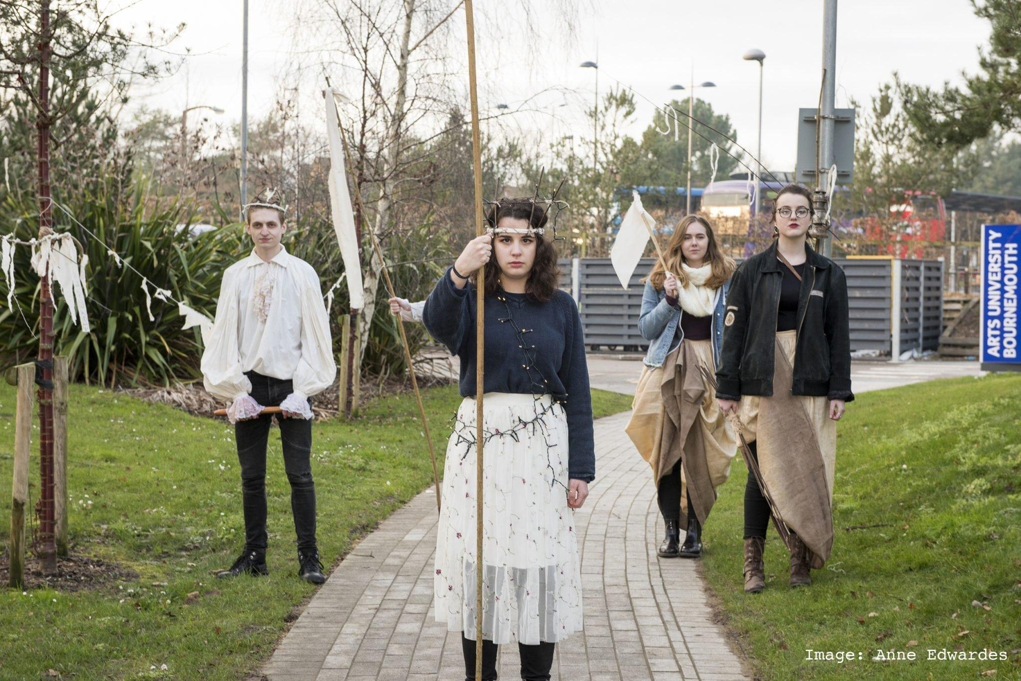 Four people in costume stand on a footpath and grass next to it