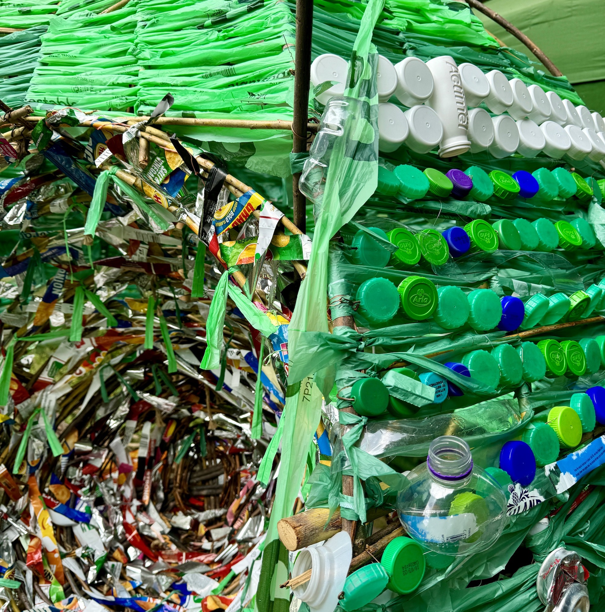 Close-up of plastic bottle caps and wrappers decorating the outside of The Anthropogenic Nest sculpture.