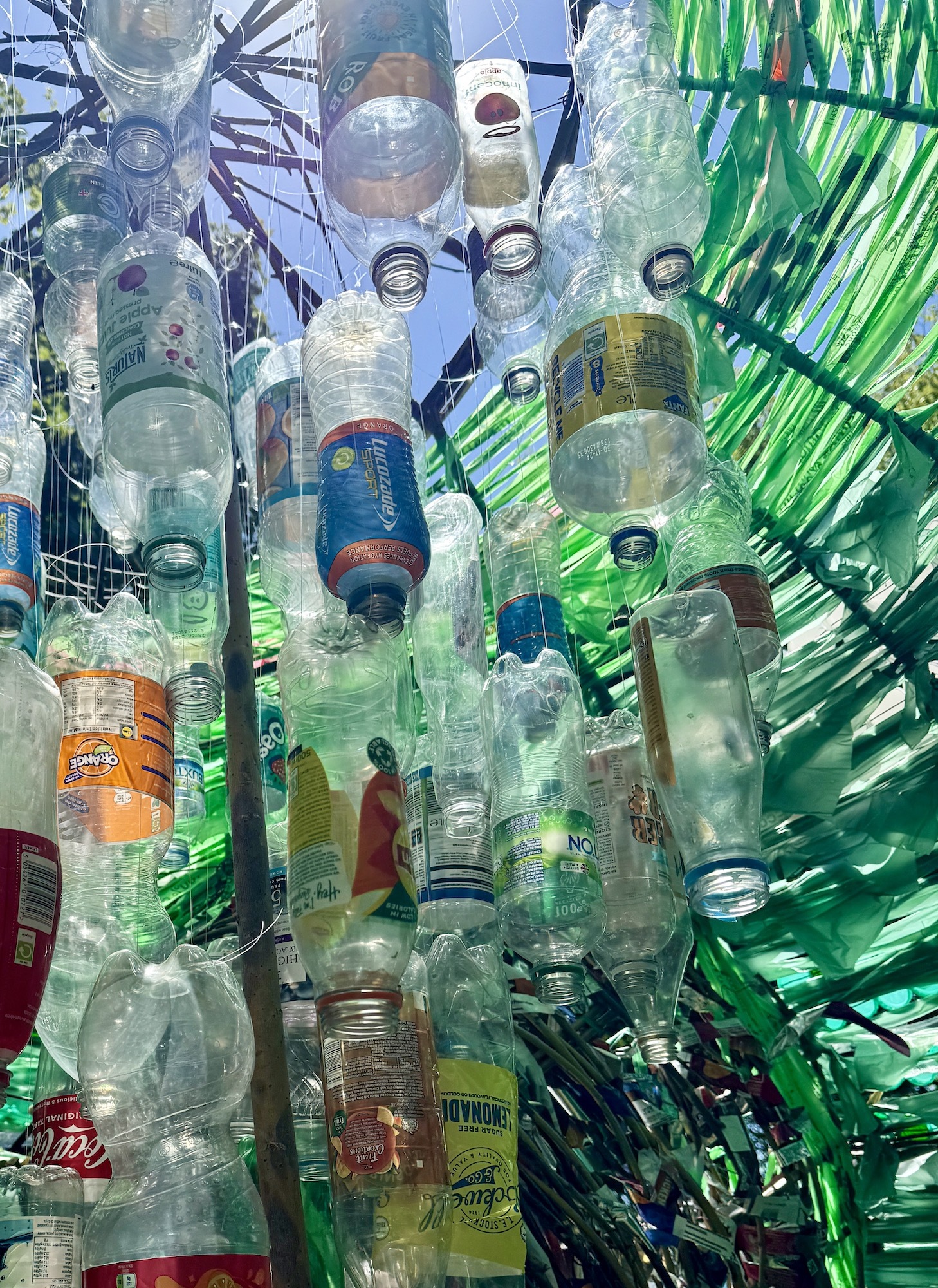 Close-up of assorted plastic bottles hanging upside-down inside The Anthropogenic Nest sculpture.