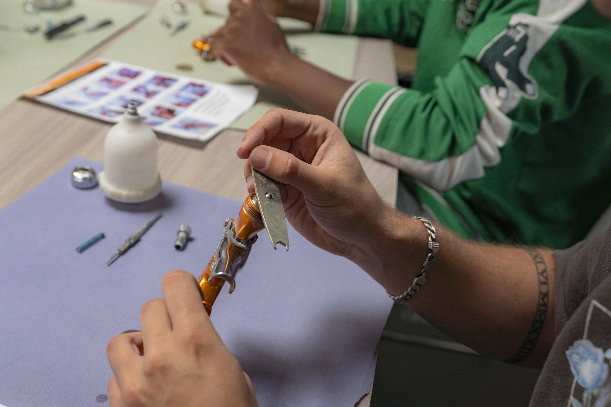 Person in green cardigan handling colourful craft materials at purple table with glue bottle and art supplies scattered around.