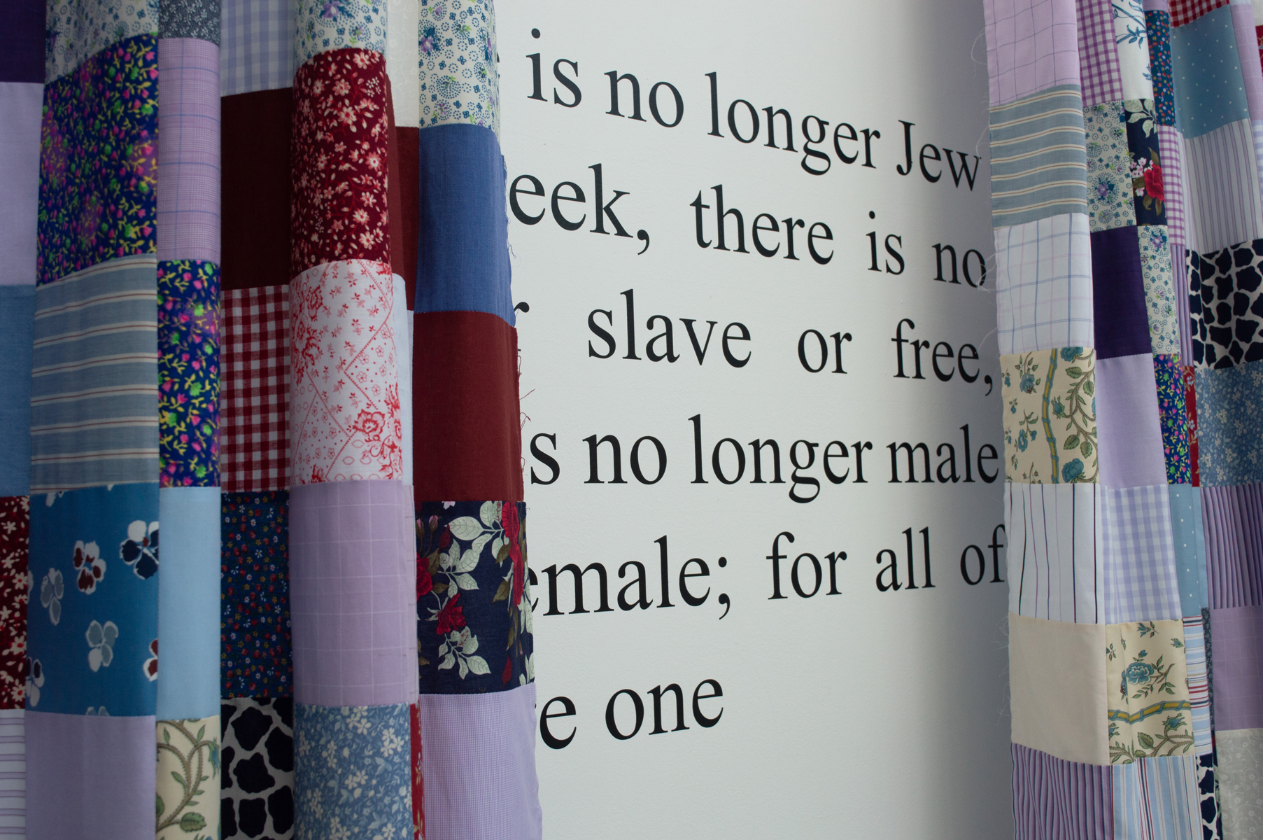 Patchwork quilt squares in blues, pinks, and florals with black text overlay reading "is no longer Jew...eek, there is no slave or free..."