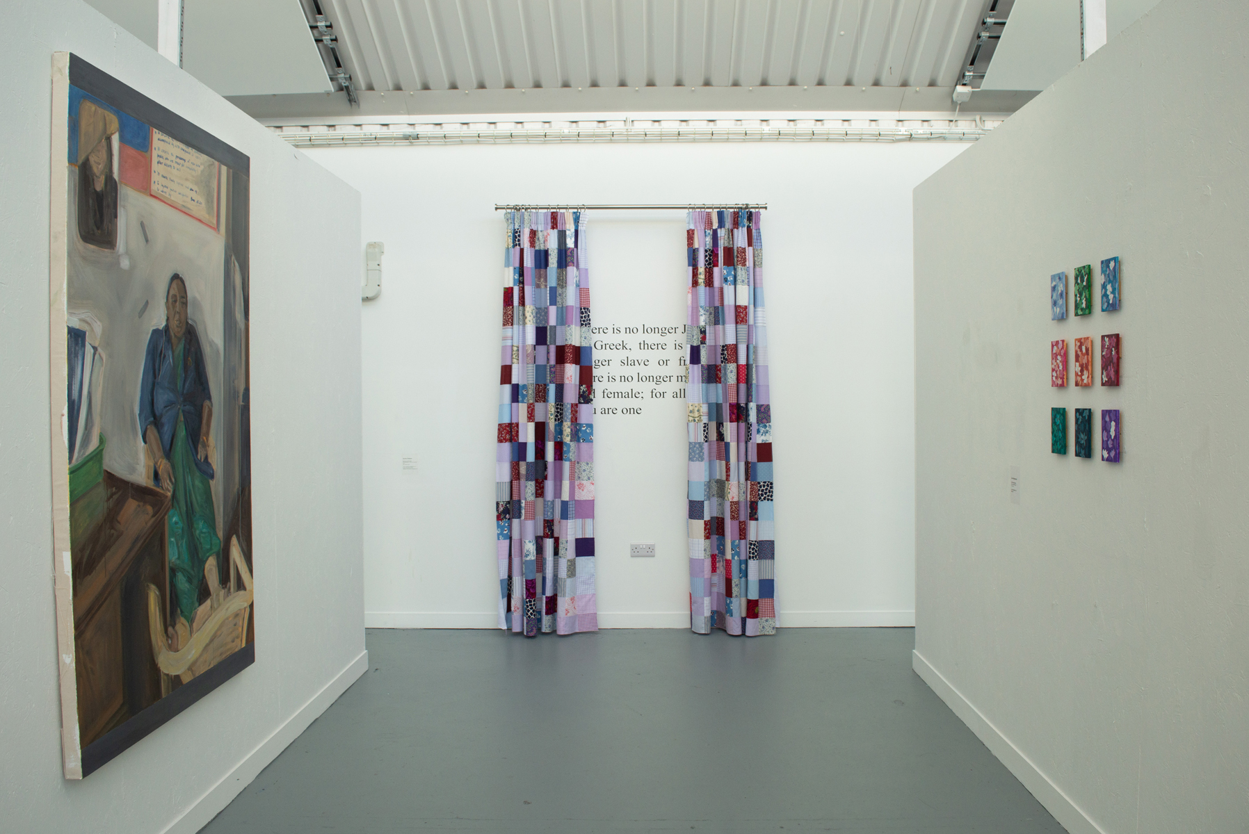 Gallery interior with white walls, grey floor, and exposed white ceiling. Artworks include large painting on left, geometric grid pieces, and multicoloured rectangular installation in centre.