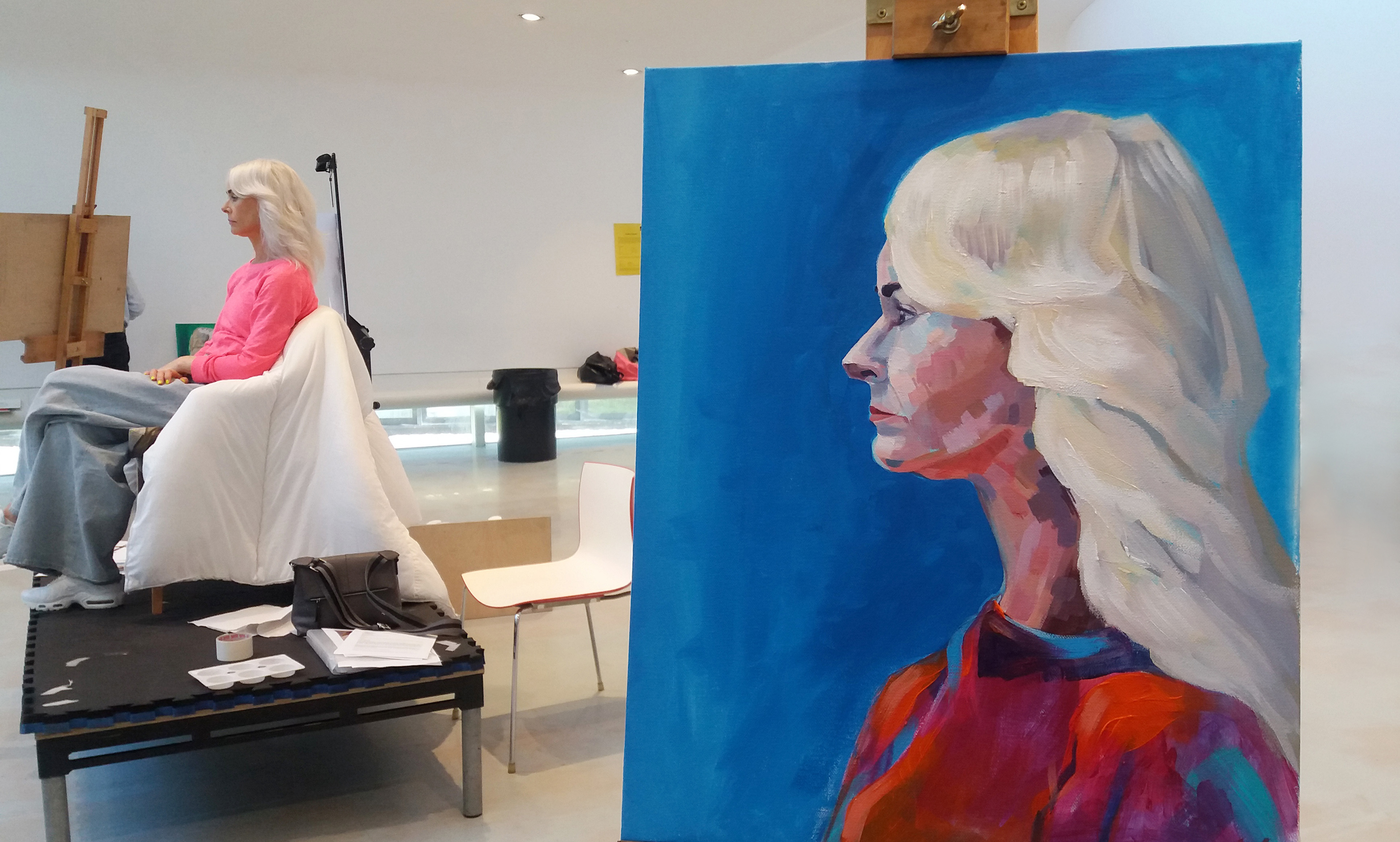 A person is posing for a life painting, the painting of the model can be seen.
