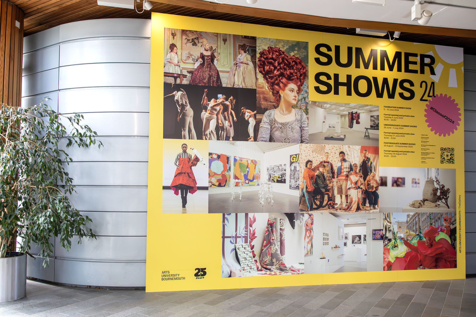 A large landscape poster with a collage of images from the AUB 2024 Summer Shows on it. The poster is standing outside a building on AUB Campus.