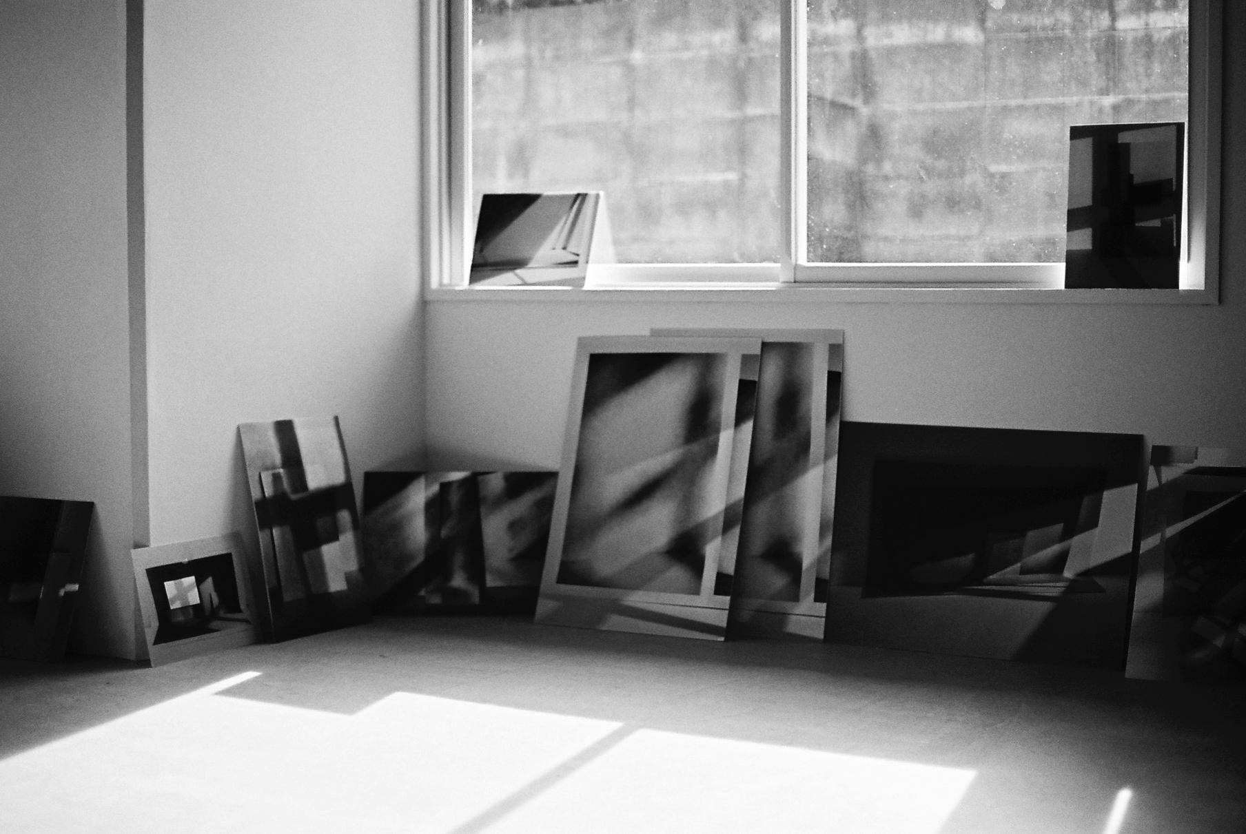 Several canvases with abstract photos on them leant up against a wall under a pair of wide windows.