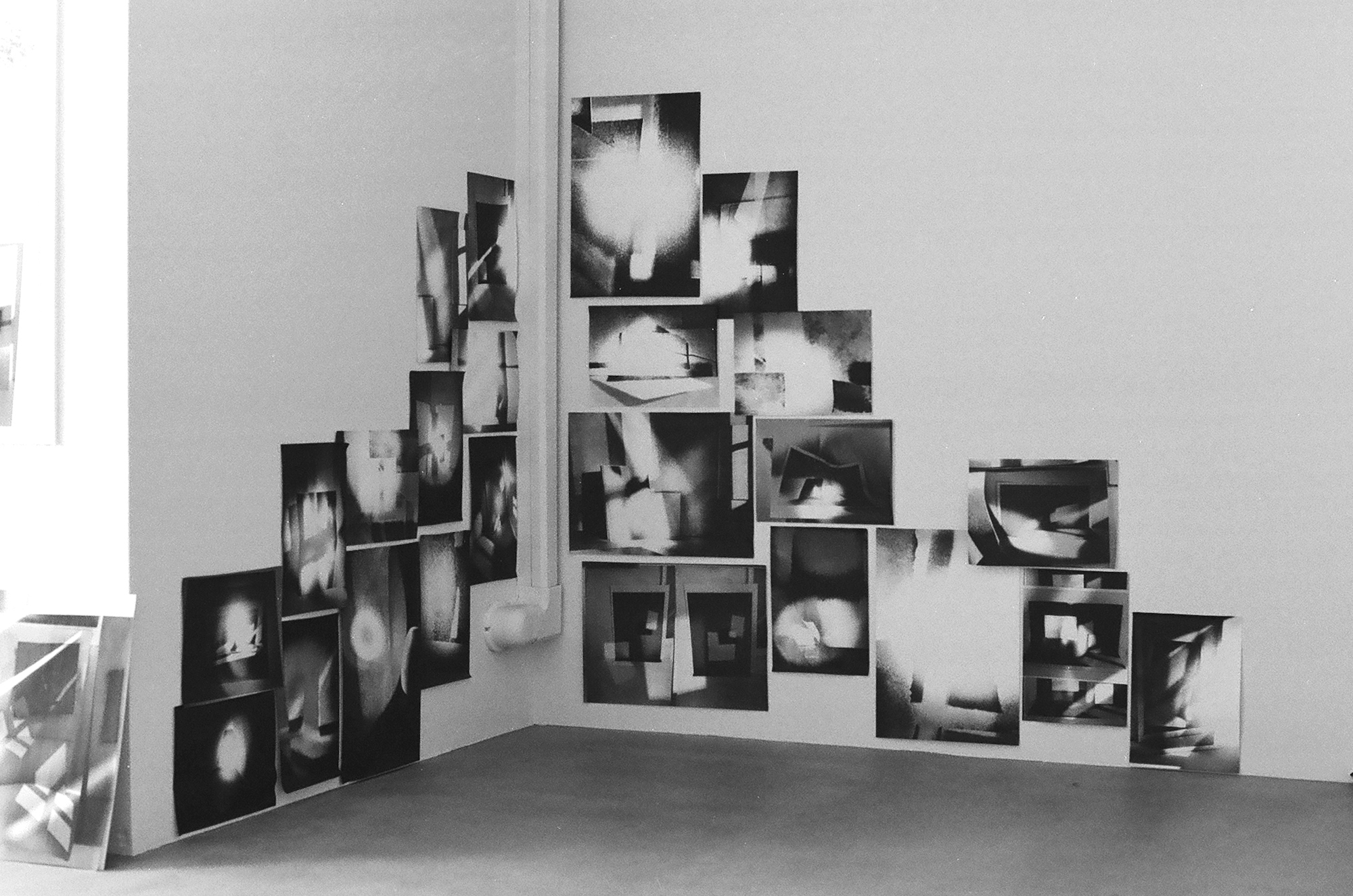 Several black and white photos stuck to a wall on top of each other.