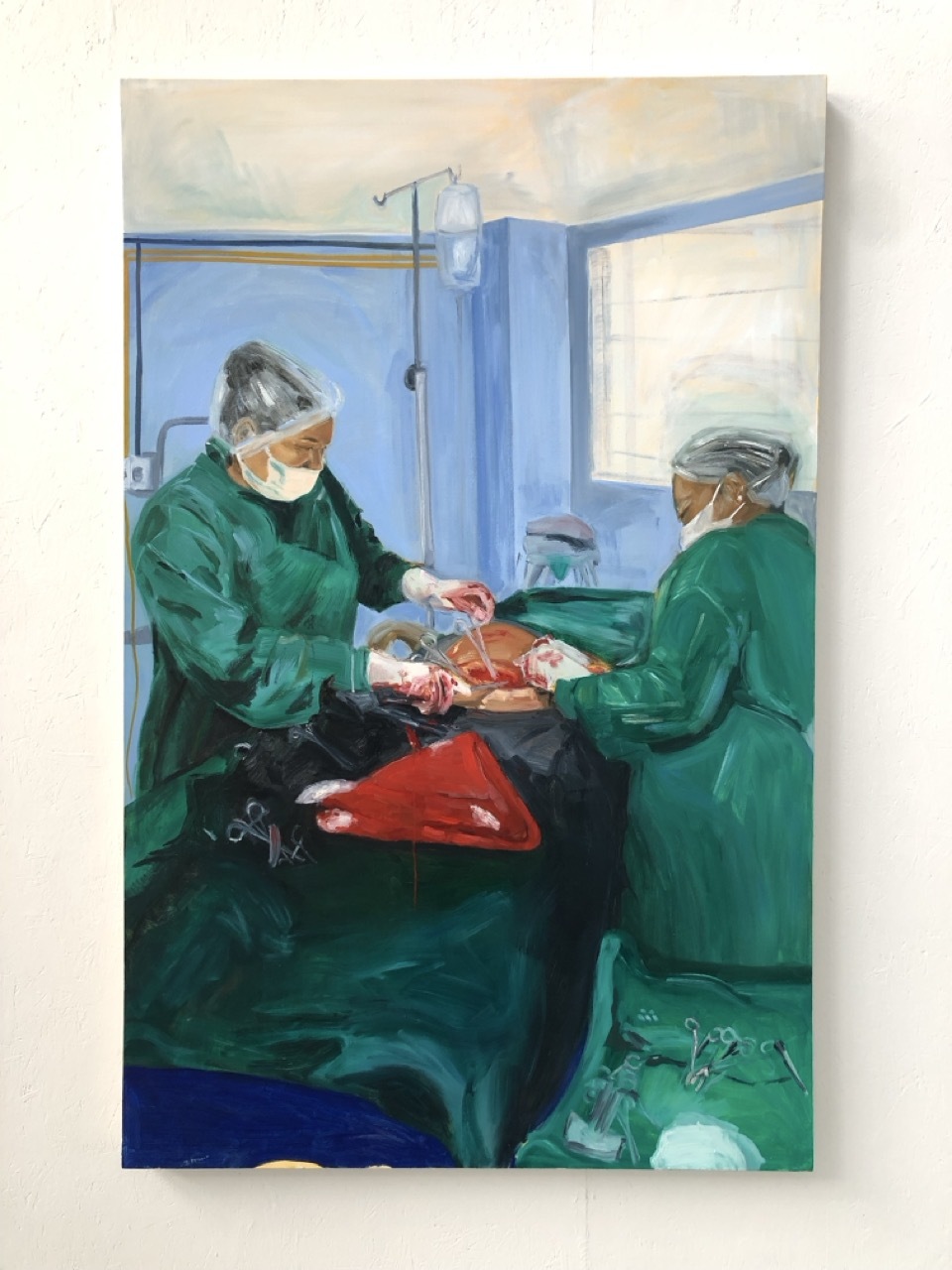 Oil painting showing two figures in green surgical gowns and masks working at a table with red elements, set in blue-walled room with window.