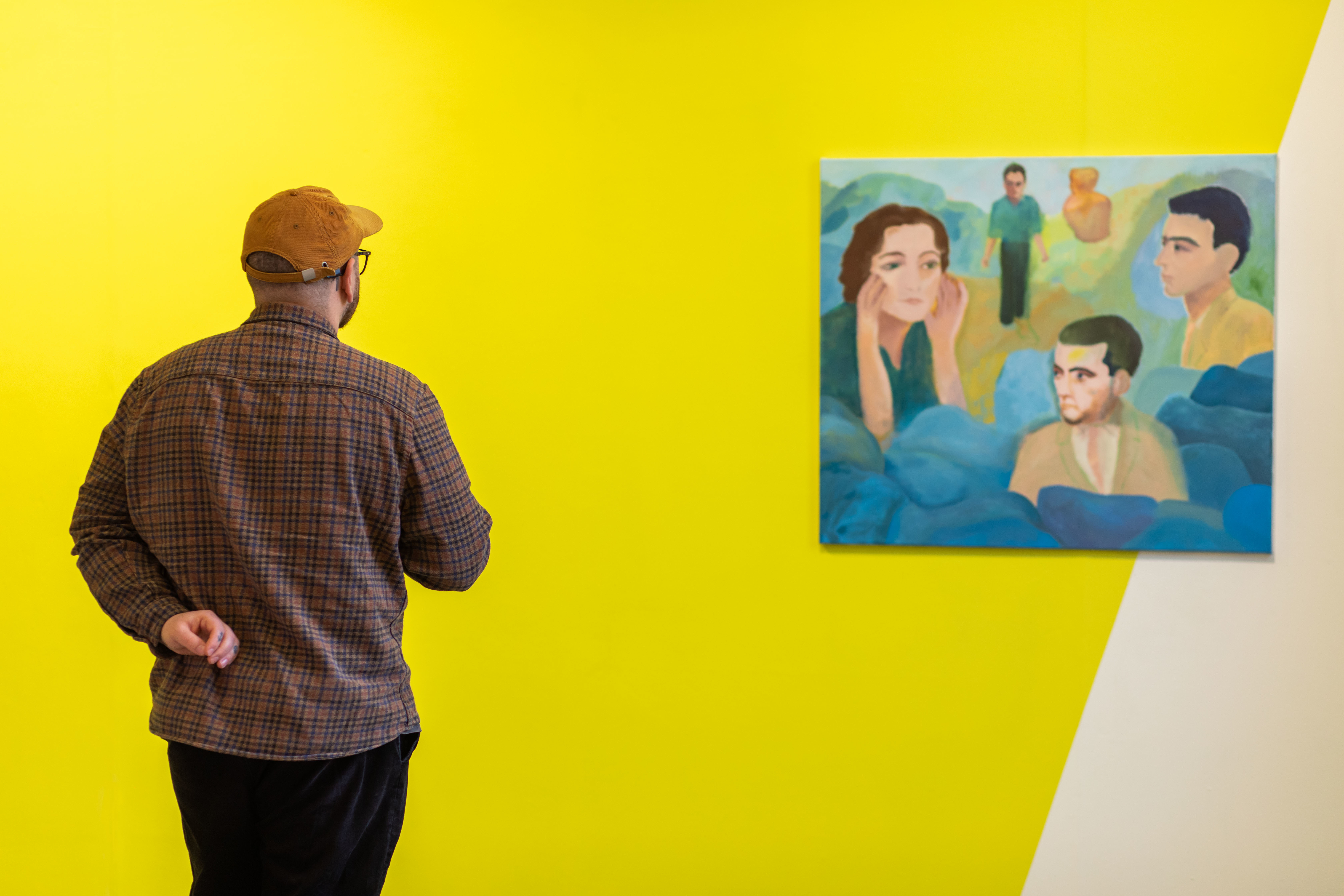 A person looking at a painting of several people, displayed on a primarily yellow wall at Aspex Portsmouth gallery.