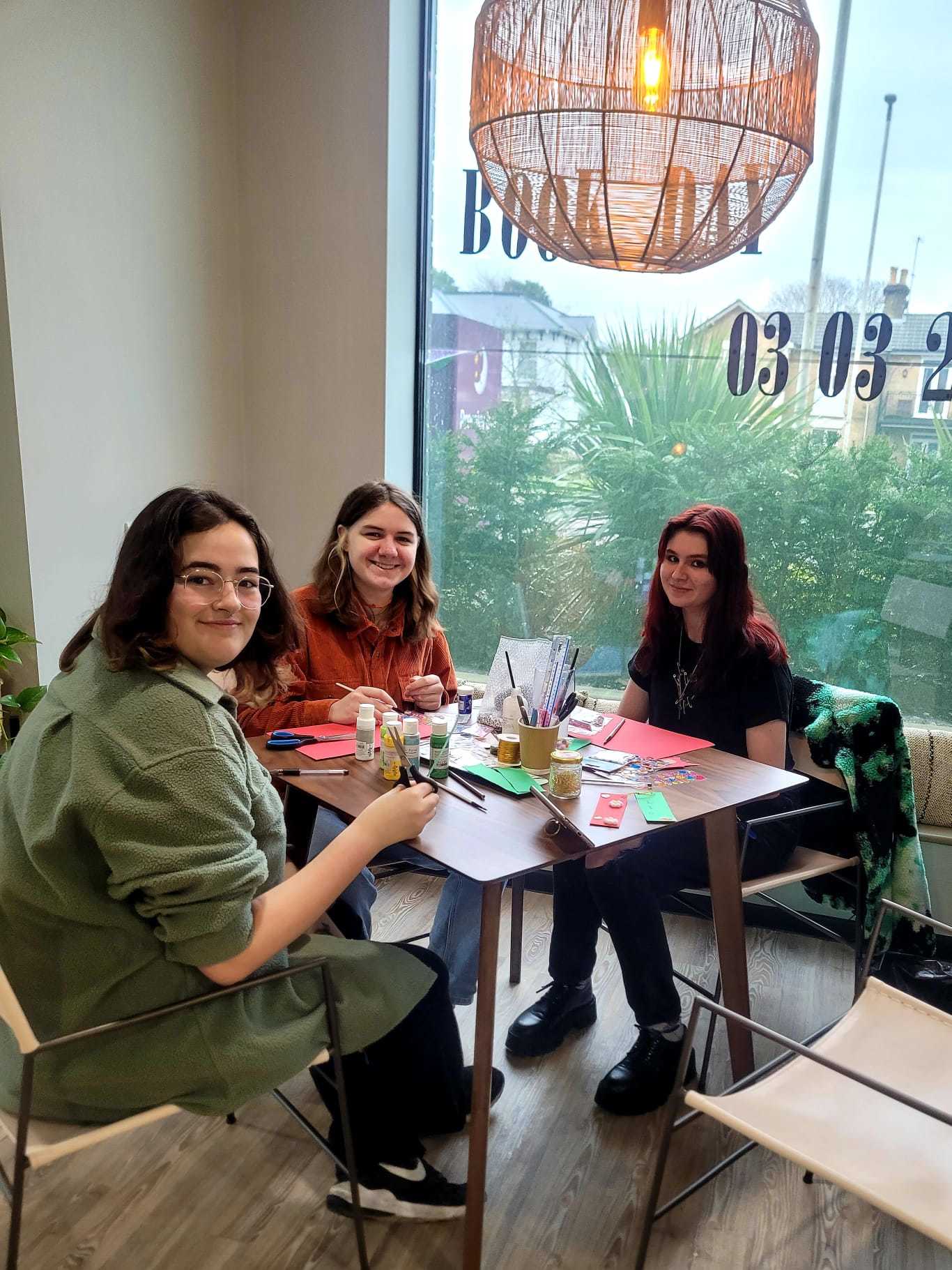A group of three students sat around a table with arts and crafts equipment in front of them.