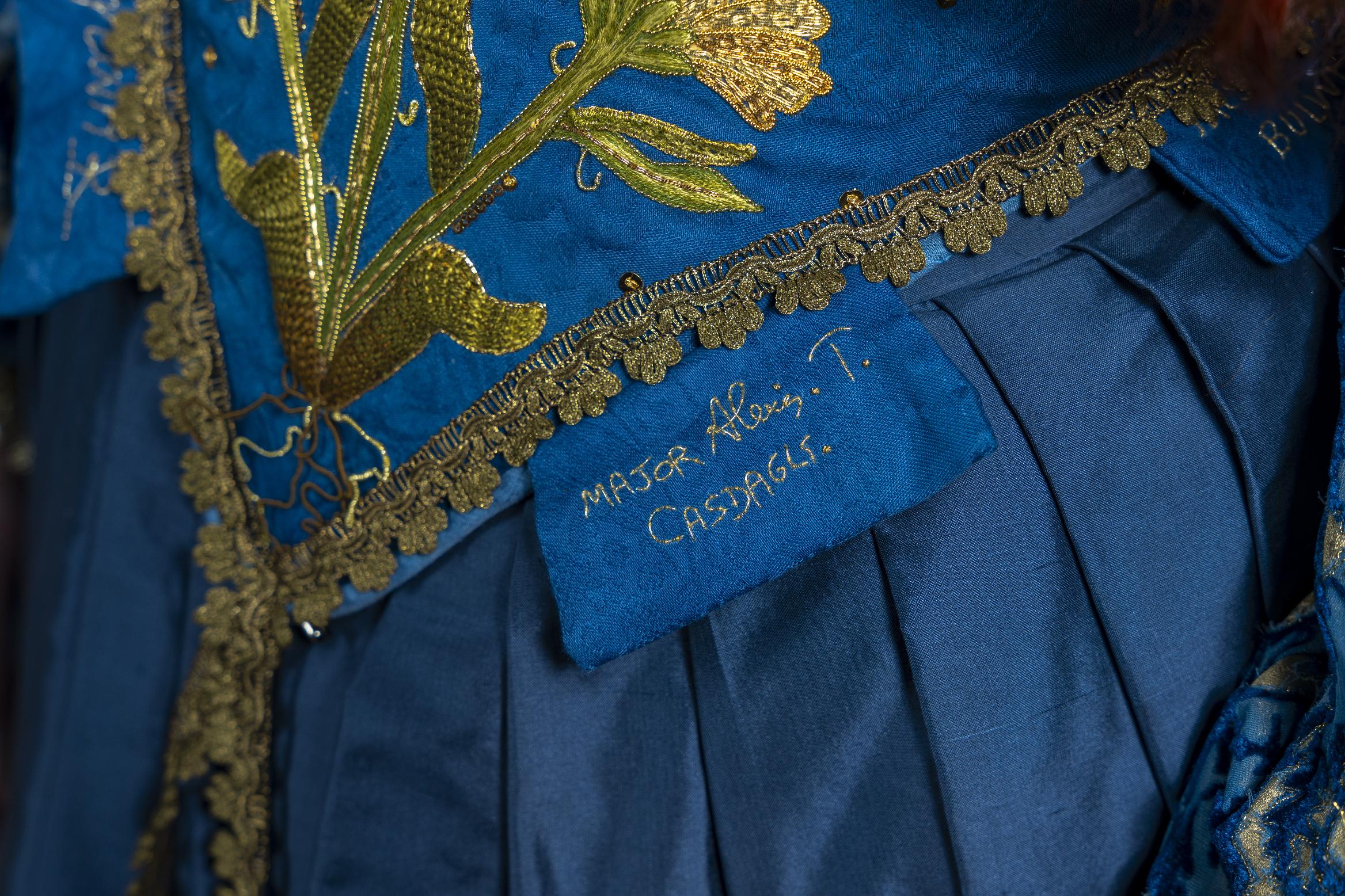 Blue embroidered dress with golden floral motif on chest, patterned blue sleeves, and gold trim details.
