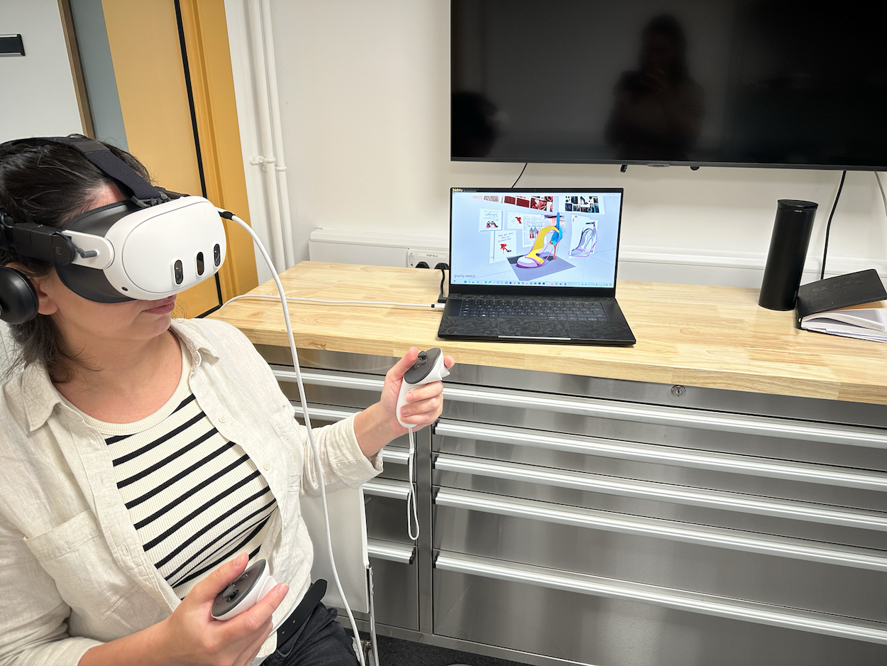 MA Digital Fashion Innovation student B Aslan using VR equipment on AUB campus, a laptop is open, showing a digital shoe design on the screen.