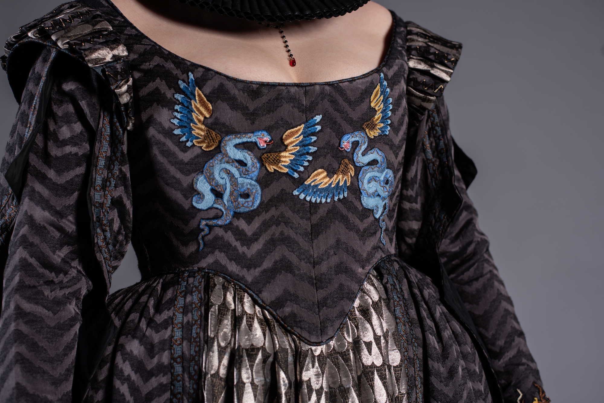 Close-up of the front of a period-style dress, with two winged snakes embroidered onto the chest.