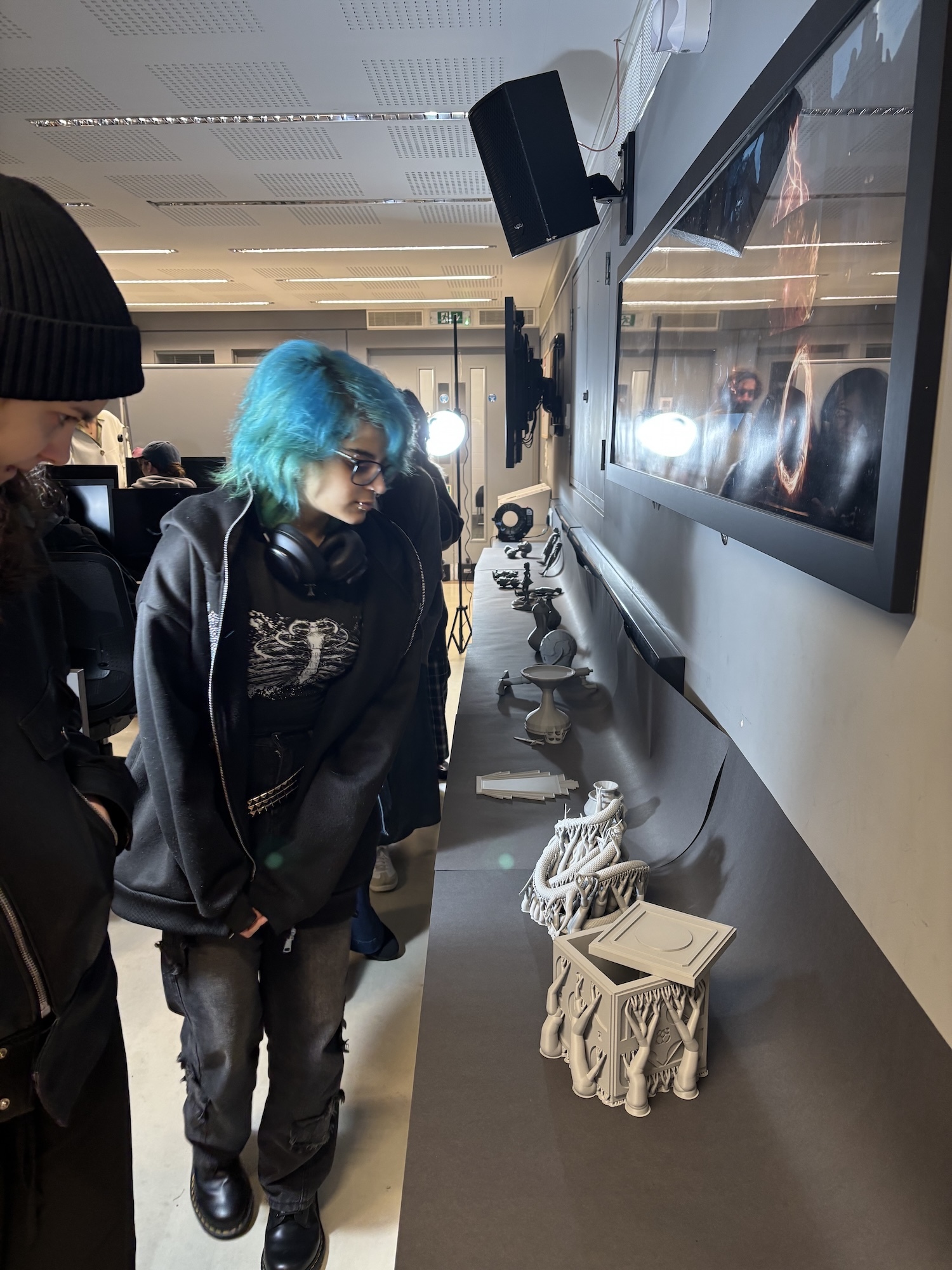 Person with bright blue hair in black hoodie walking through laboratory with microscopes and equipment on benches