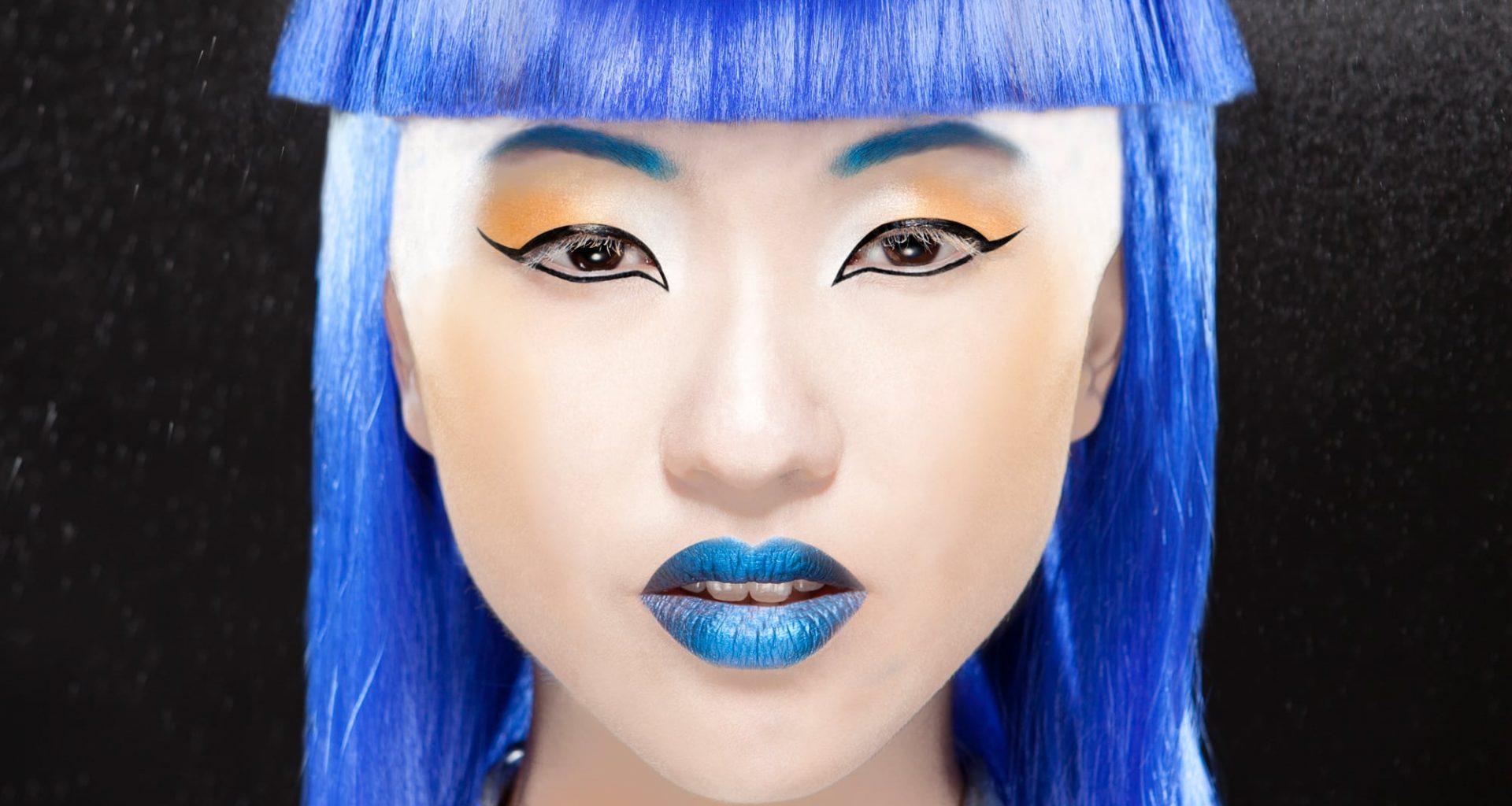 Close-up headshot of a model with blue hair, lips and eyebrows.