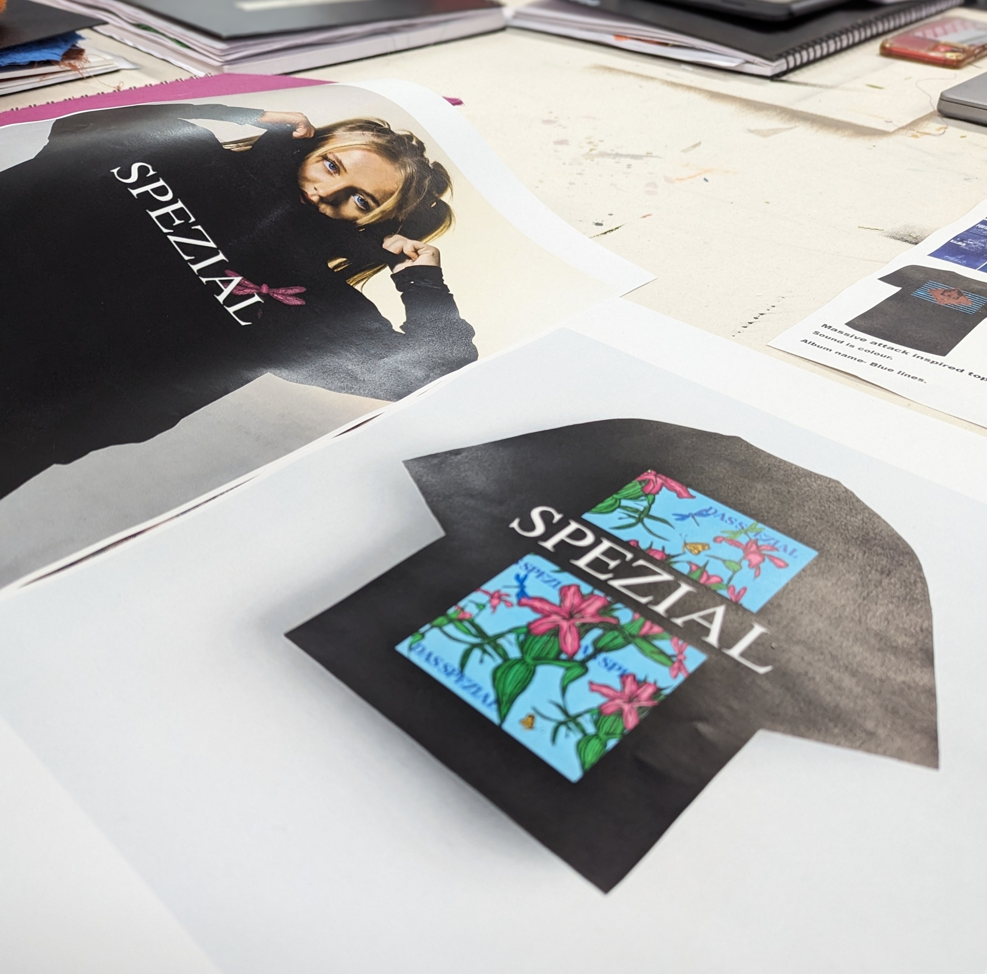 Two photos on a table, one shoes a T-shirt design with a colourful floral and insect design, the SPEZIAL logo cutting through the middle. The other shows a model wearing a black hoodie with the SPEZIAL logo and a pink dragonfly.