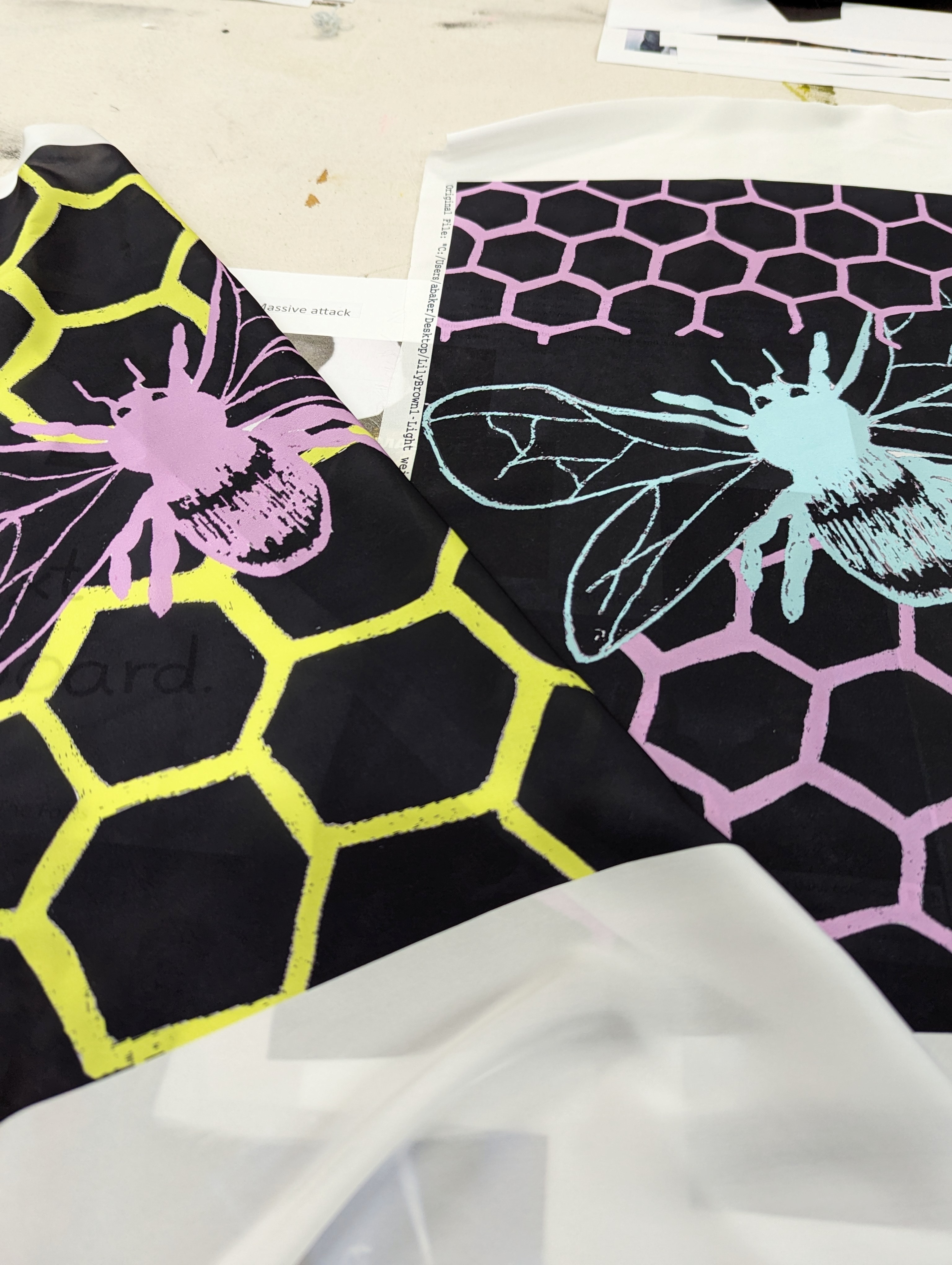 Close-up of two fabric designs, black with yellow and pink honeycomb patterns, and pink and blue icons of bees.