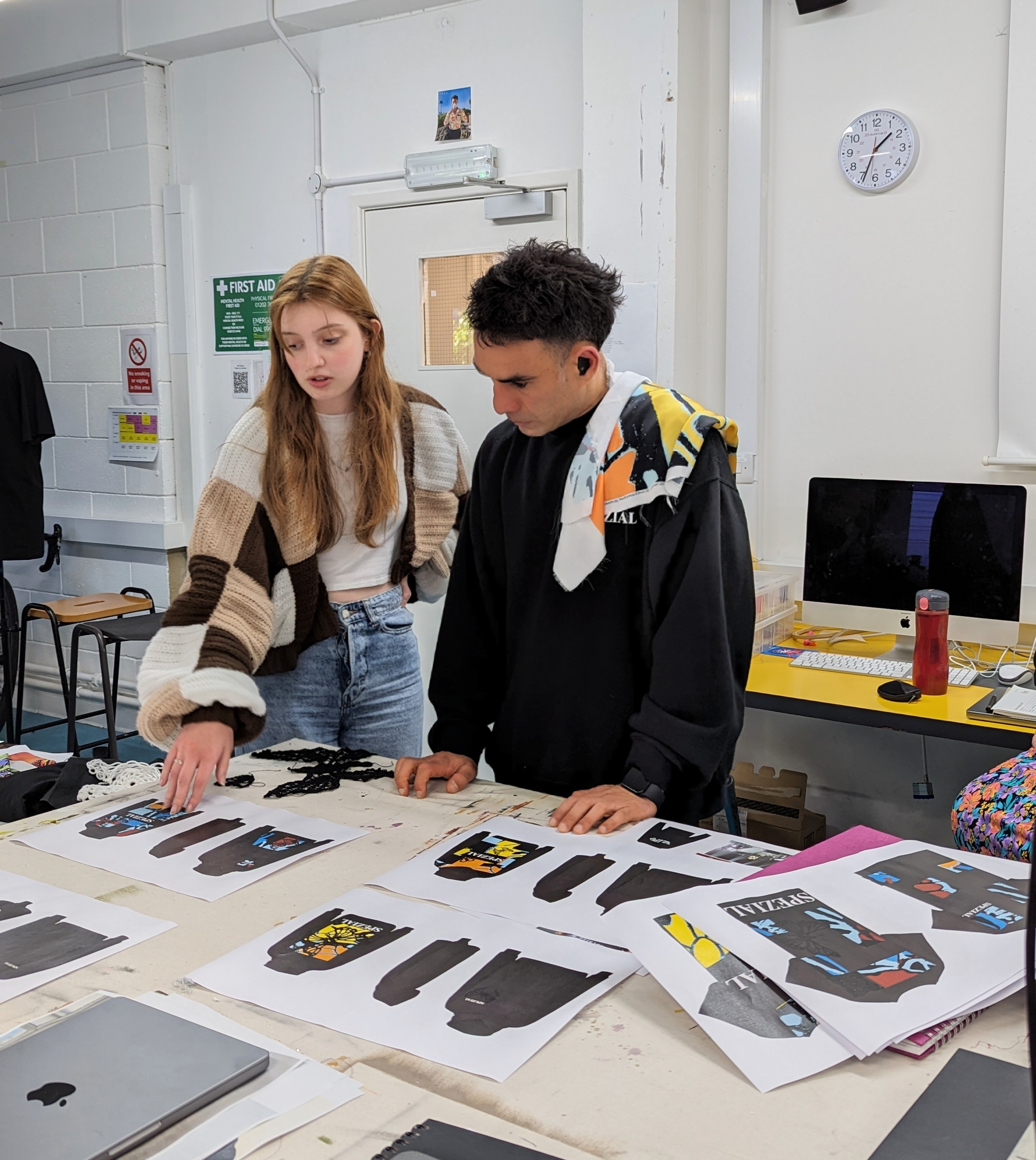 Two people standing at a table discussing various clothing designs.